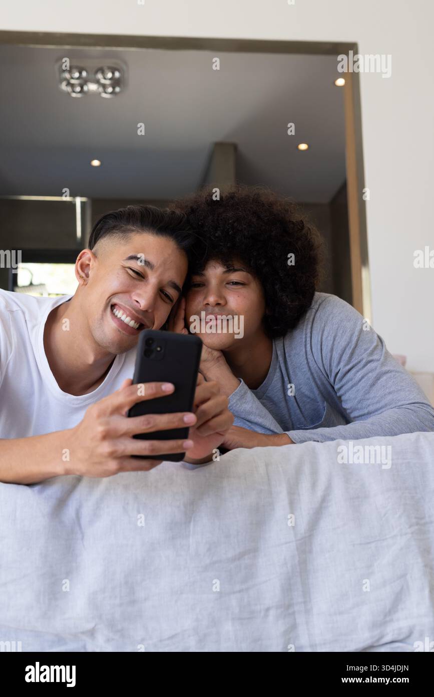 Souriant divers amis masculins allongés sur un canapé dans un salon moderne, avec smartphone et coussins Banque D'Images