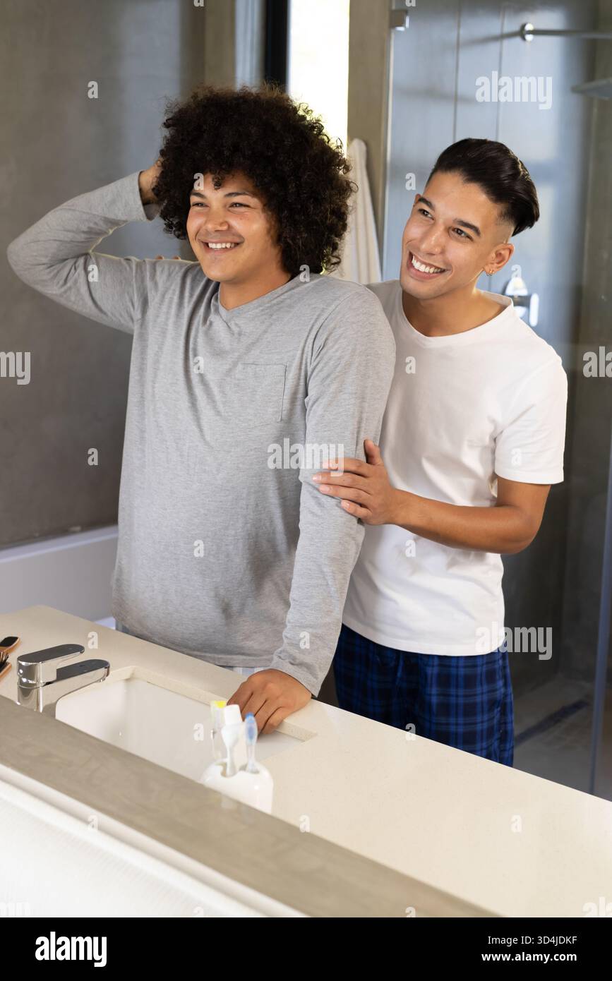 Souriant divers amis masculins debout à l'évier de salle de bain, avec porte-brosse à dents et robinet chromé Banque D'Images