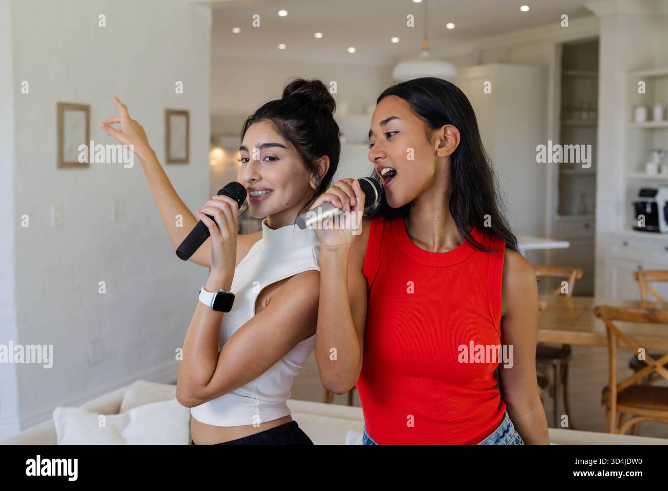Chanter diverses amies se tenant dos à dos à la maison, avec des microphones sans fil Banque D'Images