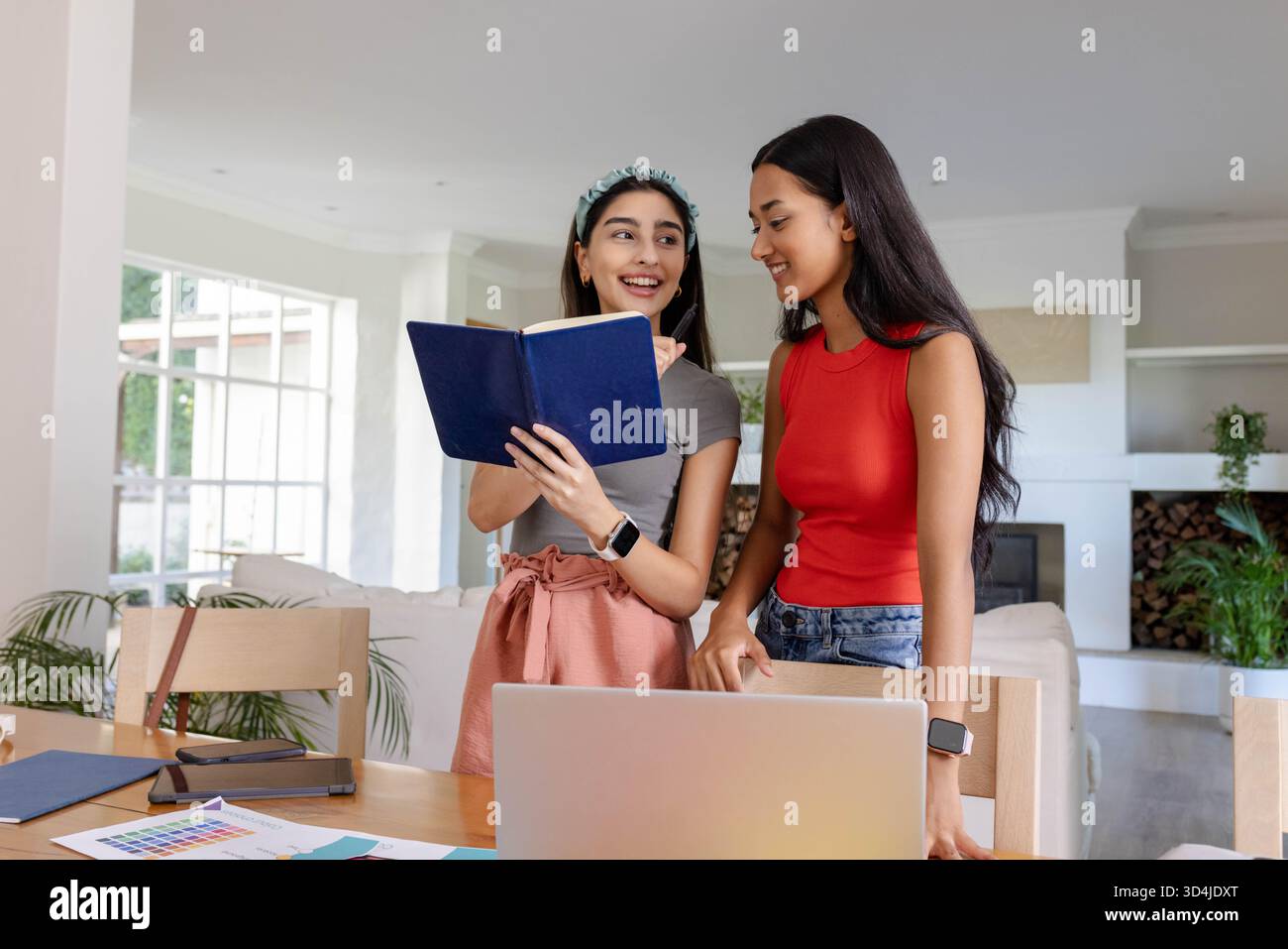 Collaborer diverses amies féminines discutant des idées à la table du salon, avec un cahier bleu Banque D'Images