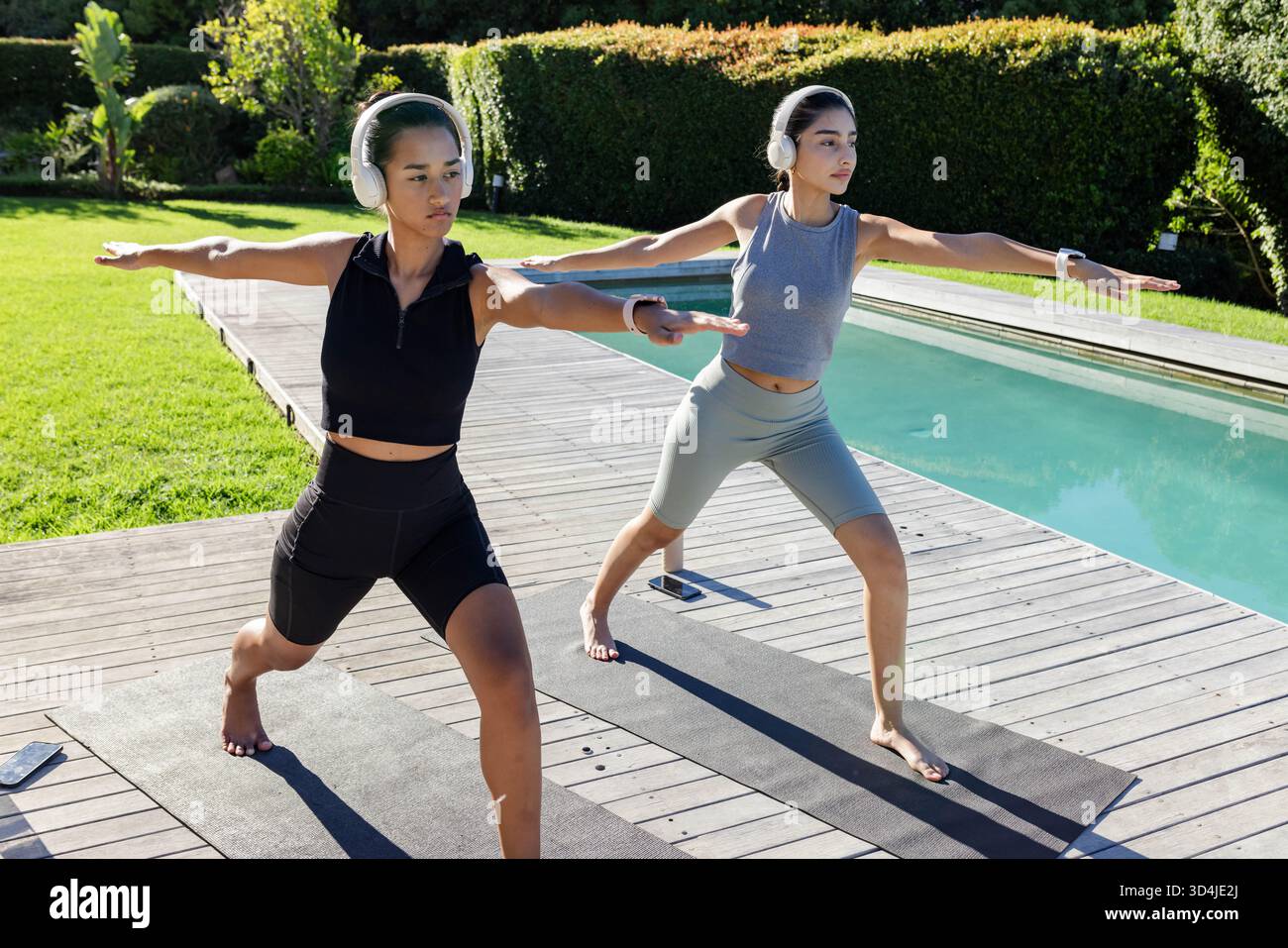 Pratiquer diverses amies féminines tenant Warrior II pose sur le pont, avec des tapis de casque smartphone Banque D'Images