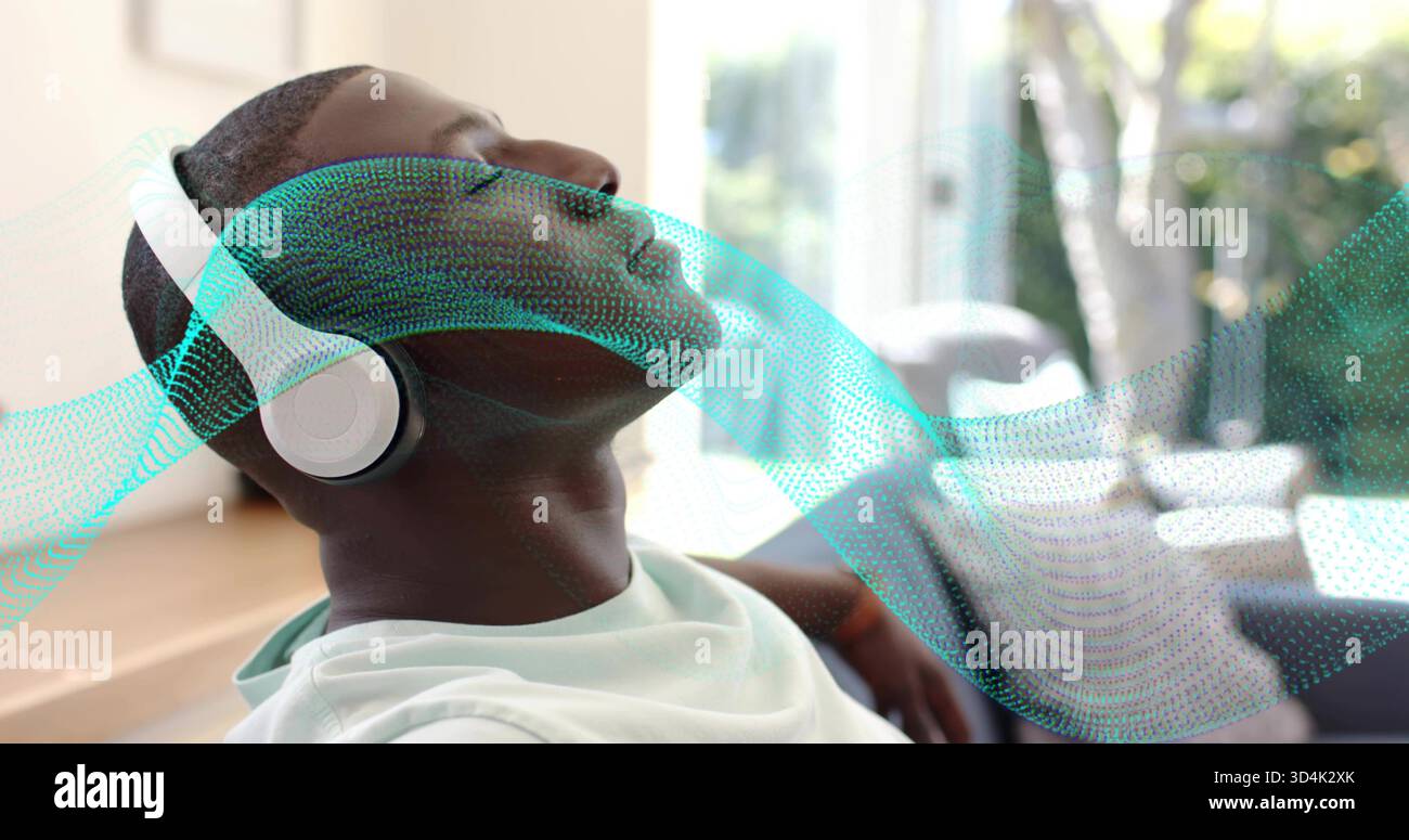 Homme inclinable portant un tee-shirt blanc et des écouteurs blancs écoutant à la maison près de la fenêtre, avec l'onde sarcelle Banque D'Images