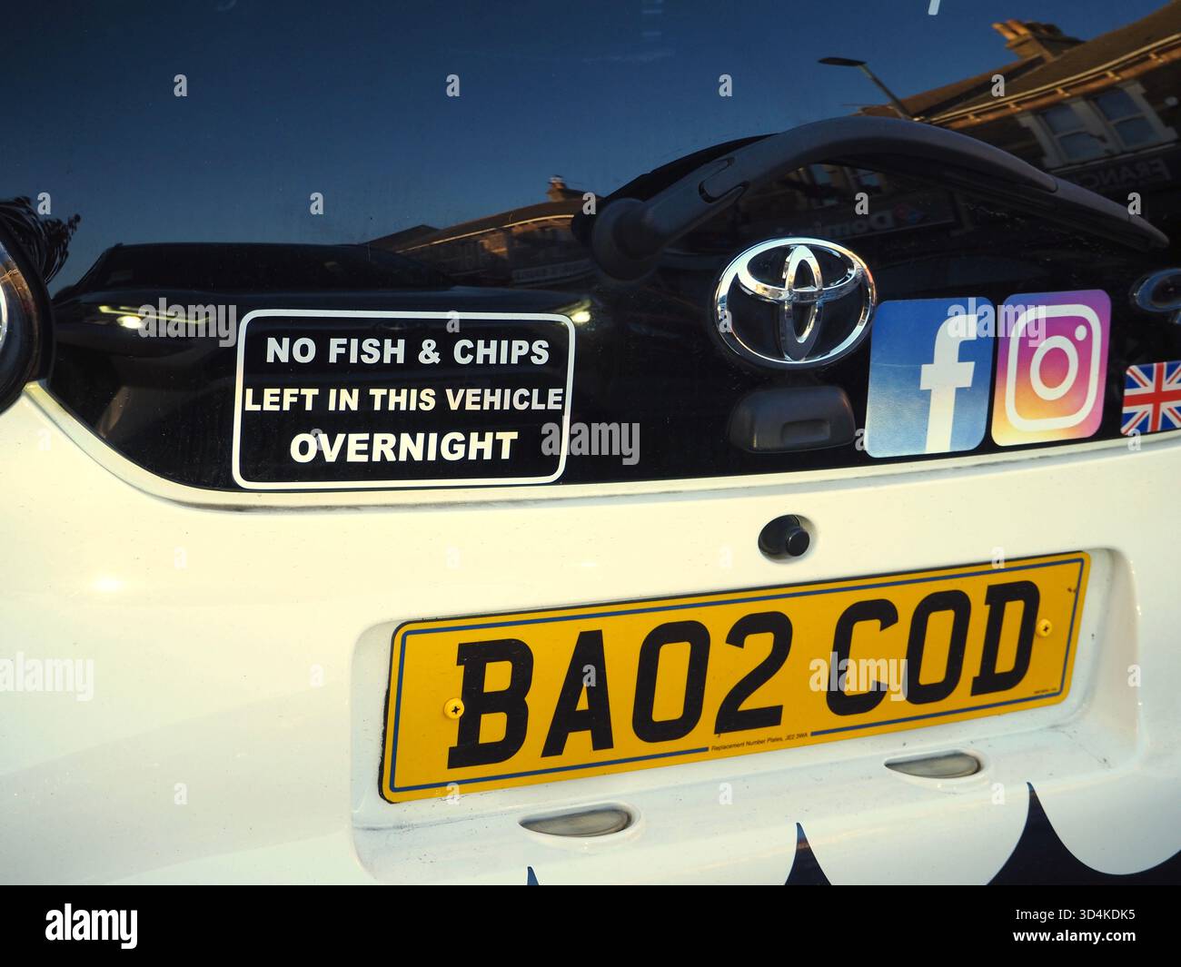 Vue arrière de la voiture de livraison de poissons et frites Toyota Aygo blanc cassé avec plaque d'immatriculation COD et autocollant « aucun poisson et frites laissé dans ce véhicule pendant la nuit » Banque D'Images