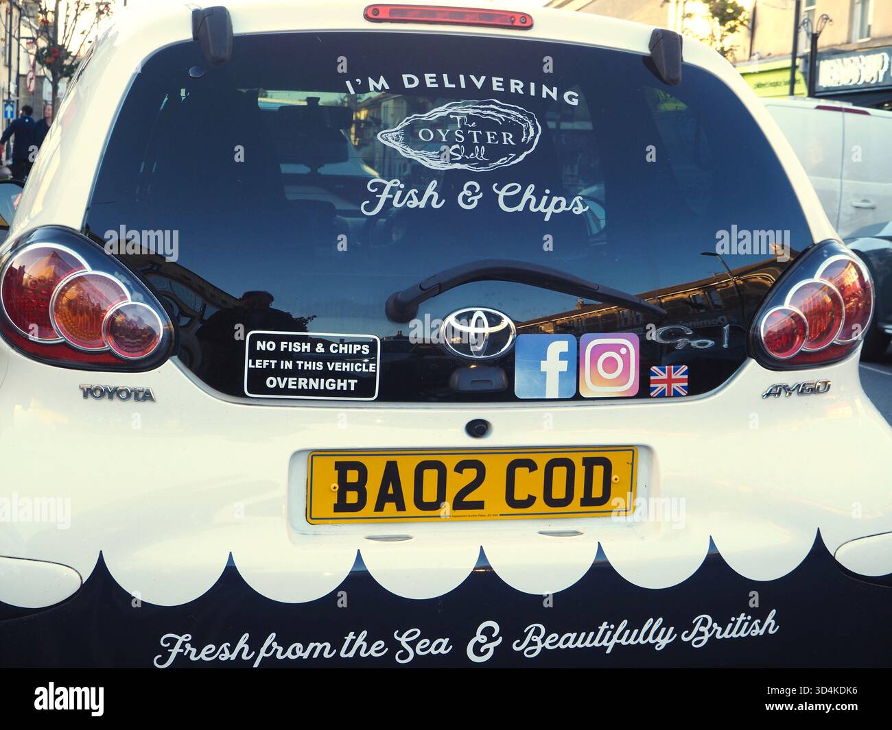 Vue arrière de la voiture de livraison de poissons et frites Toyota Aygo blanc cassé avec plaque d'immatriculation COD et autocollant « aucun poisson et frites laissé dans ce véhicule pendant la nuit » Banque D'Images