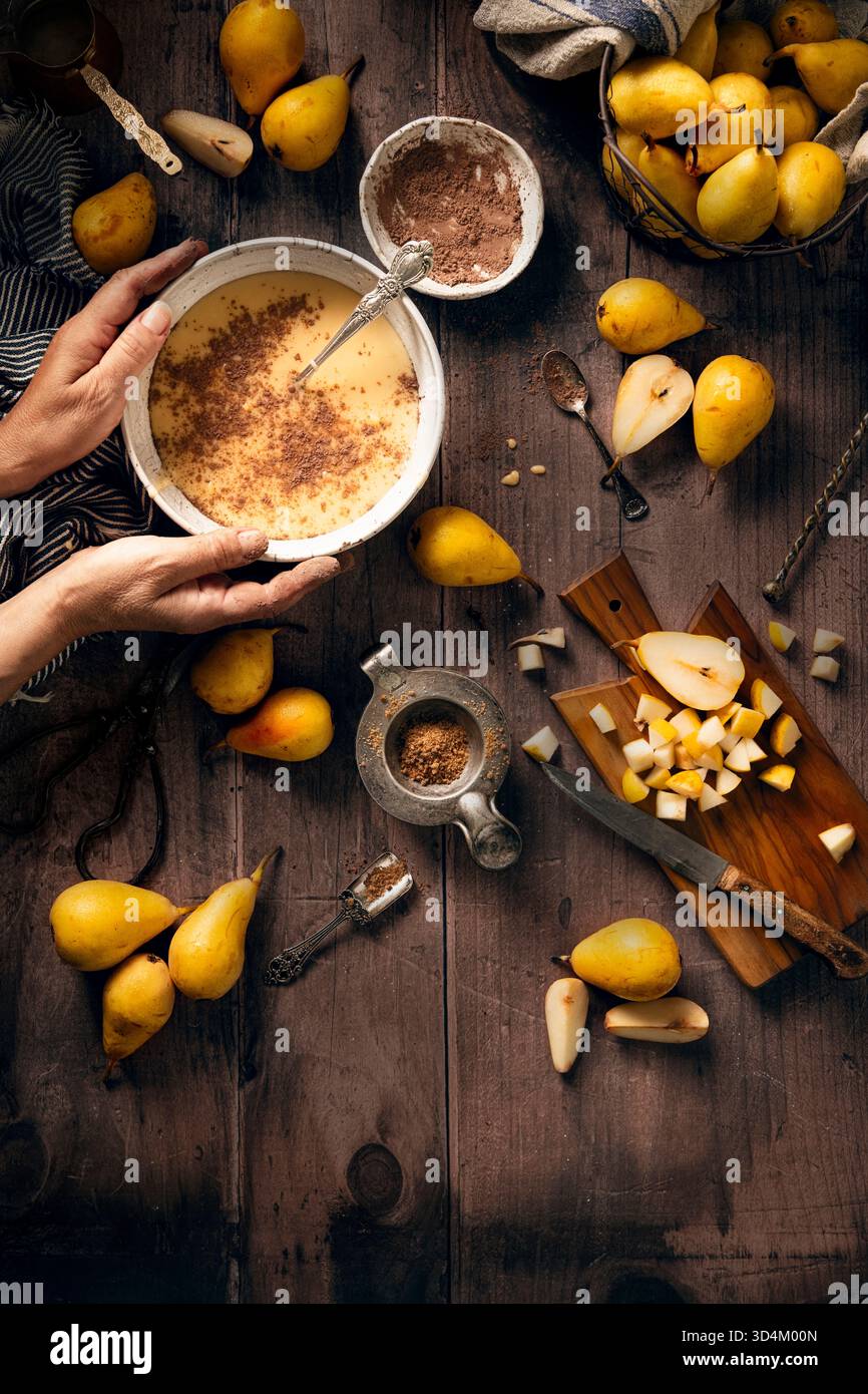 plat couche de processus de préparation d'un gâteau de poire, pâte dans un bol avec du cacao, du sucre et une planche découpée avec poire coupée en petits morceaux, quelqu'un tient t Banque D'Images