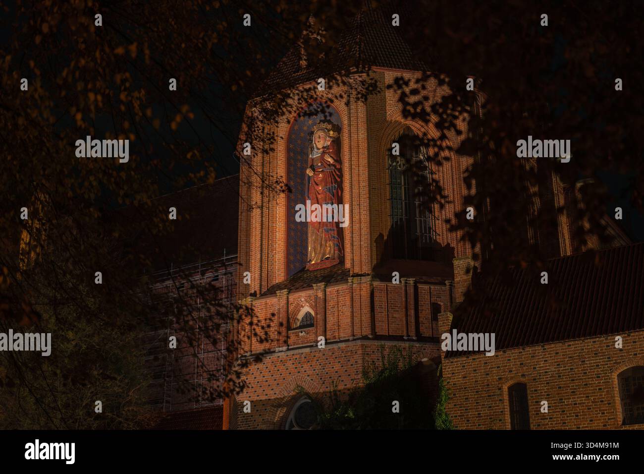 Gros plan nocturne du château de Malbork en Pologne, avec une niche en briques rouges illuminée et une grande Madone et enfant polychromes au-dessus des murs de la forteresse, des arches et Banque D'Images