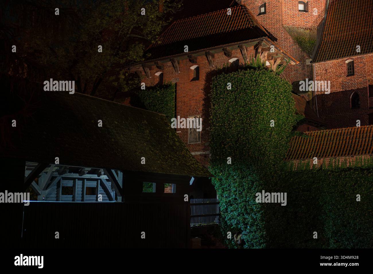 Malbork Castle en Pologne la nuit montre des murs de briques rouges, une porte à colombages, lierre sur des bastions, et des toits de tuiles abruptes, avec un faible éclairage dramatique et Banque D'Images