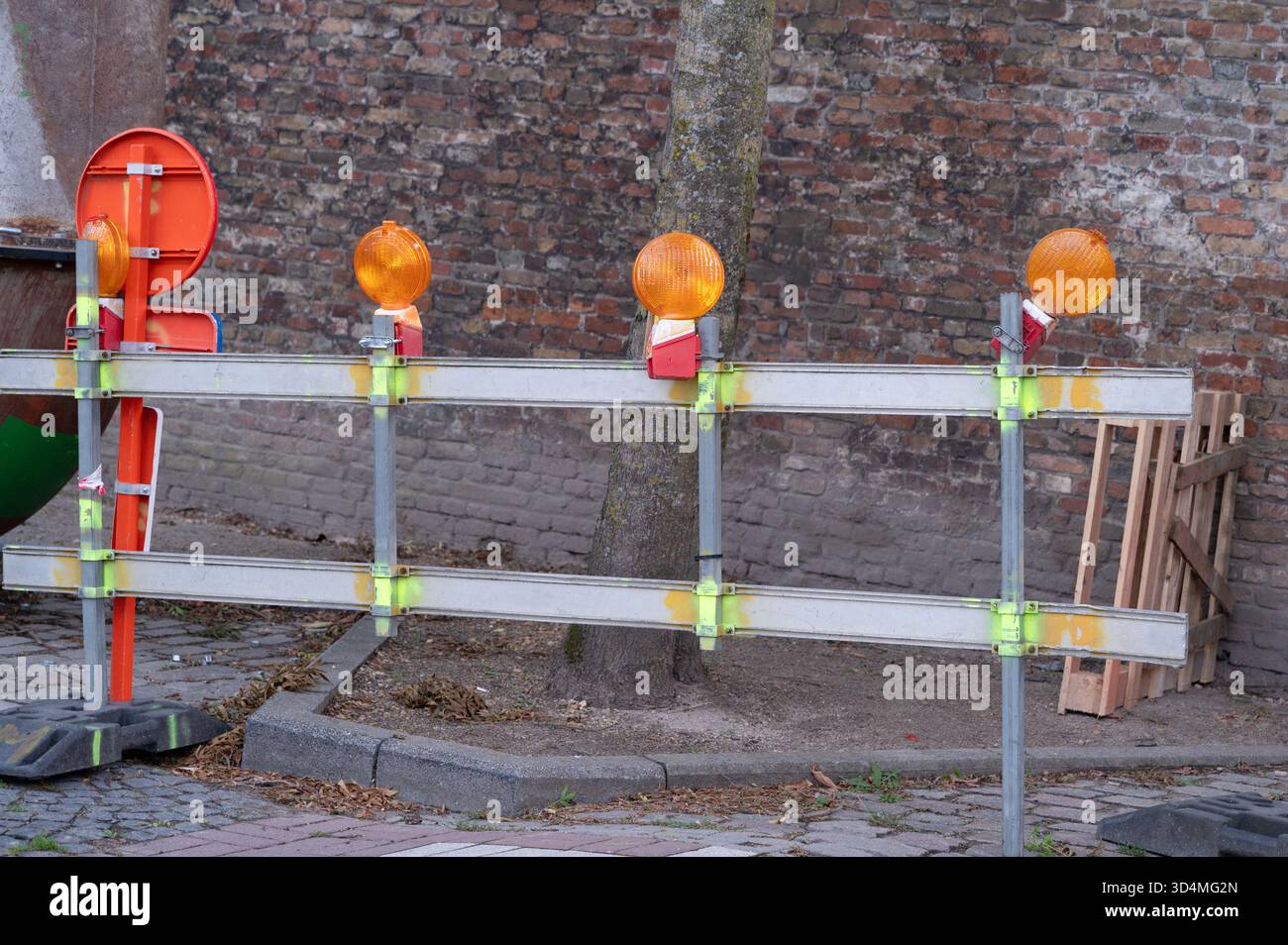 Barricade routière temporaire avec feux orange, laissée par l'équipe municipale préparant la réparation de la chaussée à côté du mur de briques et des palettes empilées, marqueurs réfléchissants Banque D'Images