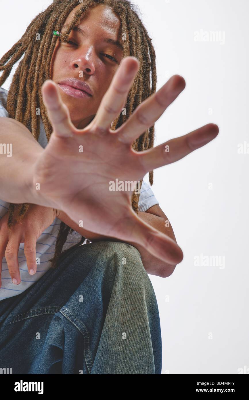 Jeune homme avec des dreadlocks bras tendus et main ouverte vers le spectateur en studio Banque D'Images