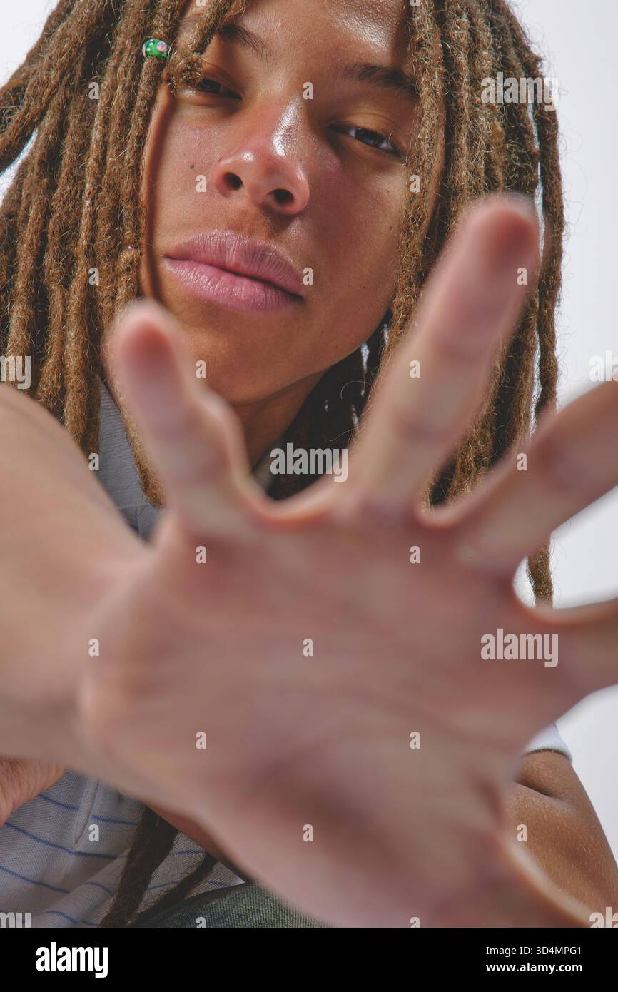 Jeune homme avec des dreadlocks bras tendus et main ouverte vers le spectateur en studio Banque D'Images
