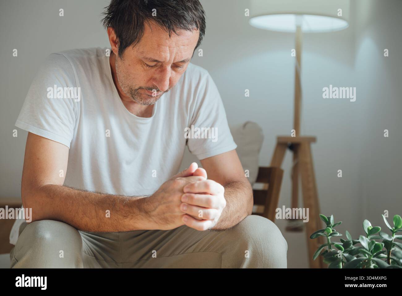 Homme solitaire décontracté avec une expression tristement et regrettable assis à l'intérieur, se sentant déprimé et perdu dans la pensée dans un salon confortable sombre Focus sélectif. Banque D'Images