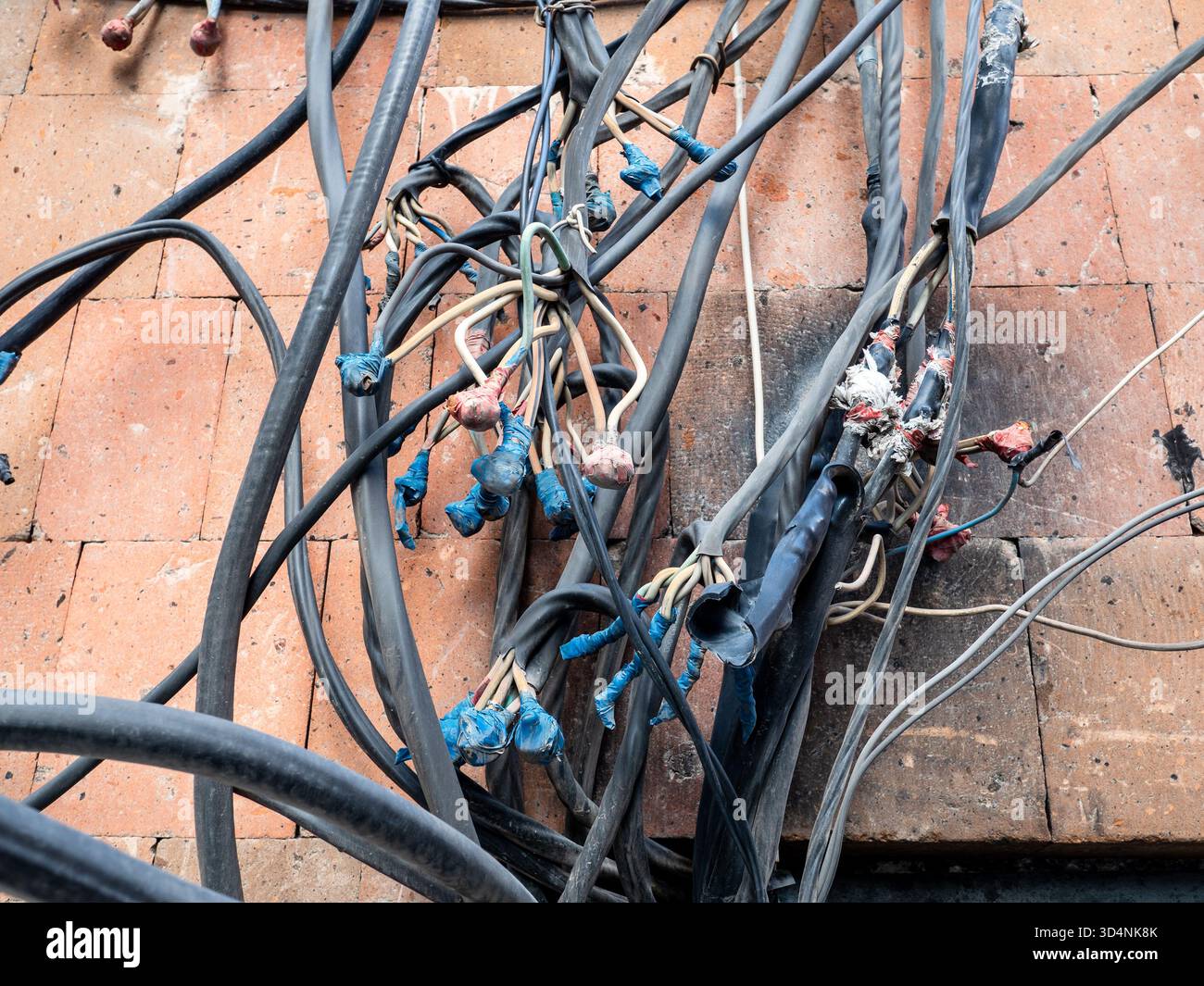 Câbles électriques chaotiquement enchevêtrés du câblage externe sur le mur de la maison en pierre de tuf rose dans la ville d'Erevan, Arménie au crépuscule de l'automne Banque D'Images
