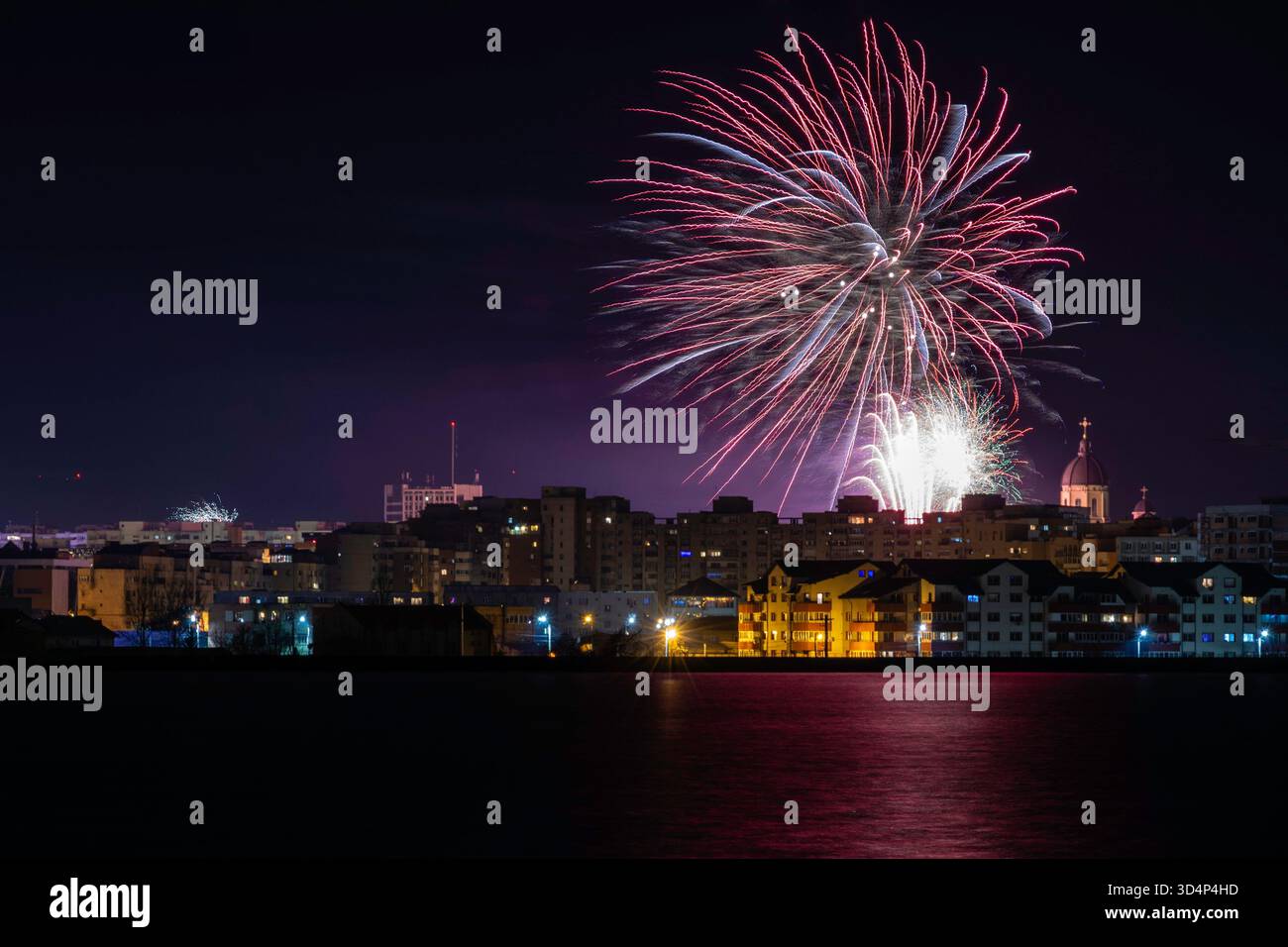 Feux d'artifice rouges, blancs et bleus au-dessus de la ville illuminée avec le dôme de l'église. Un moment festif dramatique. Banque D'Images