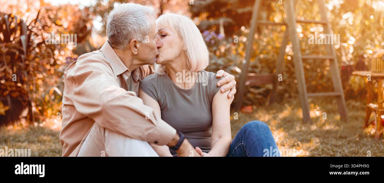 Couple âgé partage un baiser tendre dans un jardin ensoleillé pendant l'automne Banque D'Images