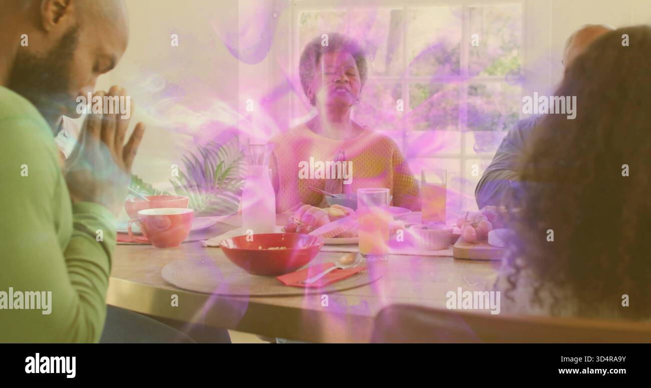 Femme priant portant un pull moutarde menant la prière à la table à manger à la maison, avec des bols rouges Banque D'Images