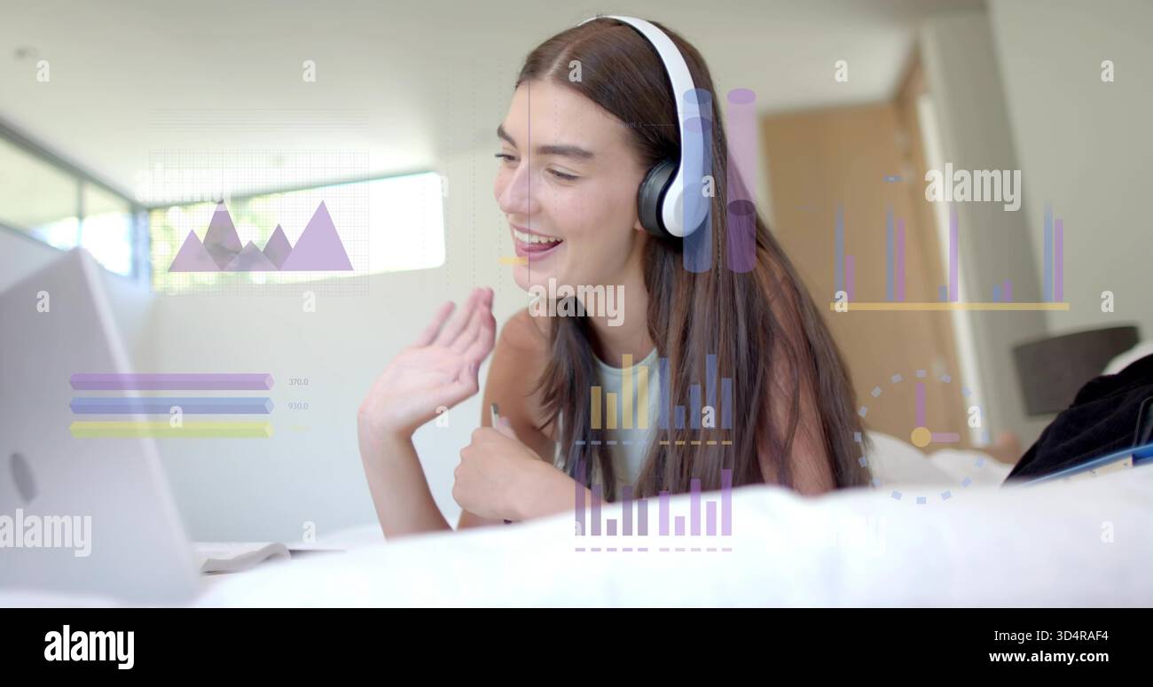 Agitant femme couchée dans la chambre portant le dessus sans manches, casque, en utilisant un ordinateur portable avec des graphiques de données Banque D'Images