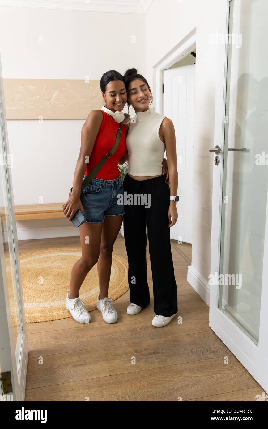Embrasser diverses amies debout dans l'entrée de la maison, avec smartphone et écouteurs Banque D'Images