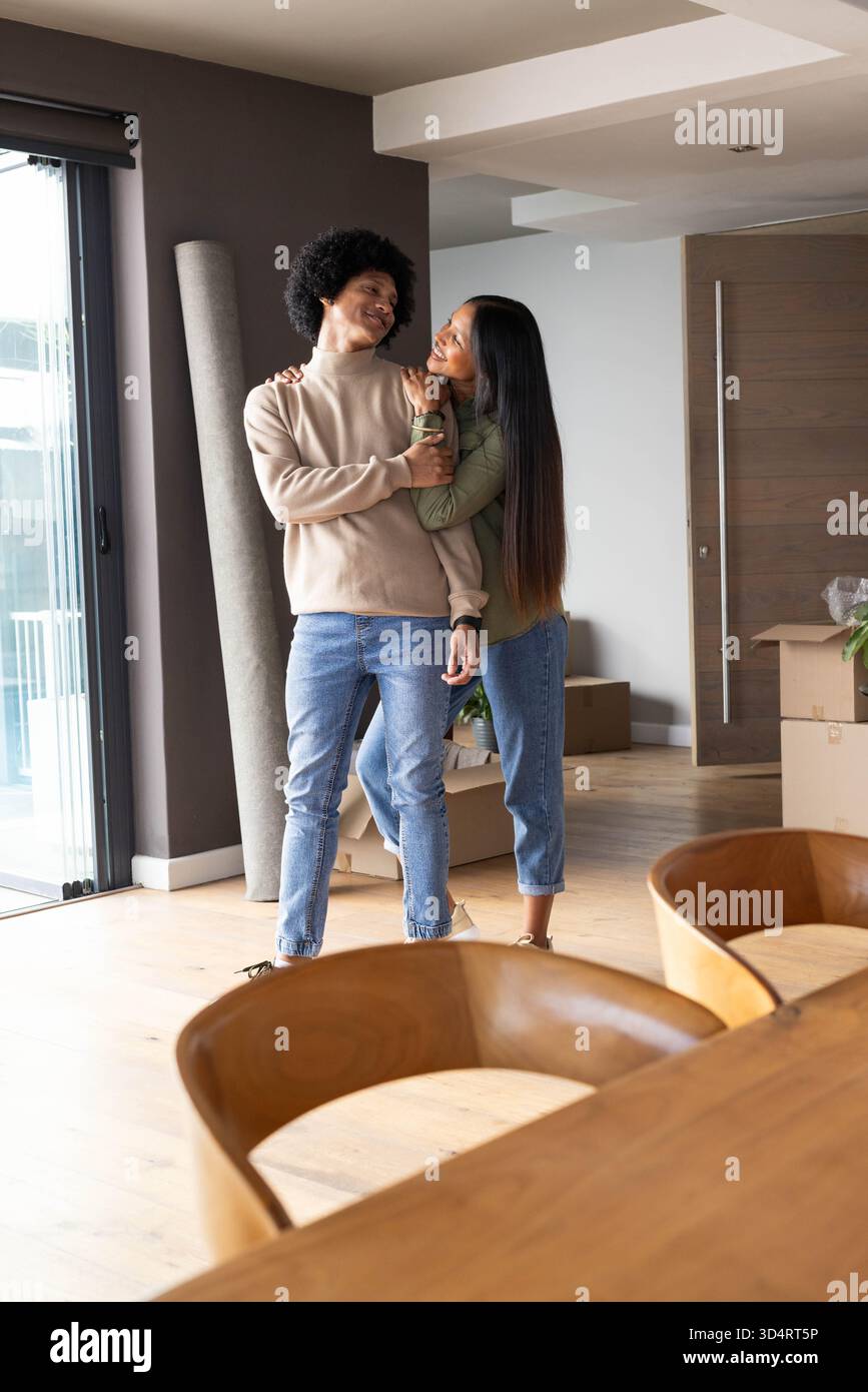 Couple diversifié debout et souriant dans le salon moderne, avec des boîtes mobiles et tapis roulé Banque D'Images
