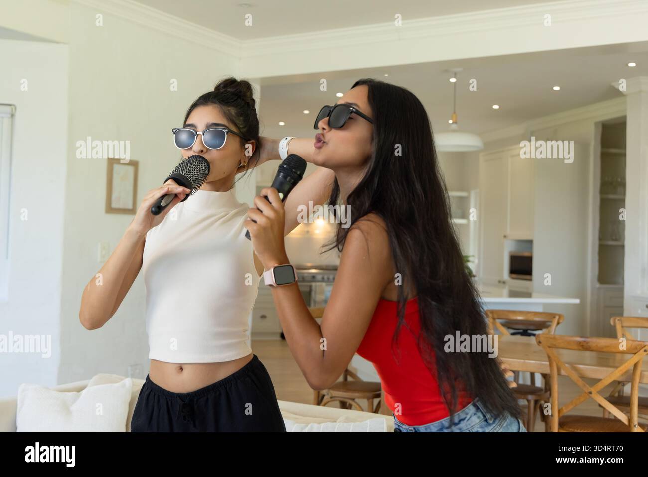 Diverses amies chantant dans des microphones sans fil dans un salon ouvert, avec des lunettes de soleil Banque D'Images