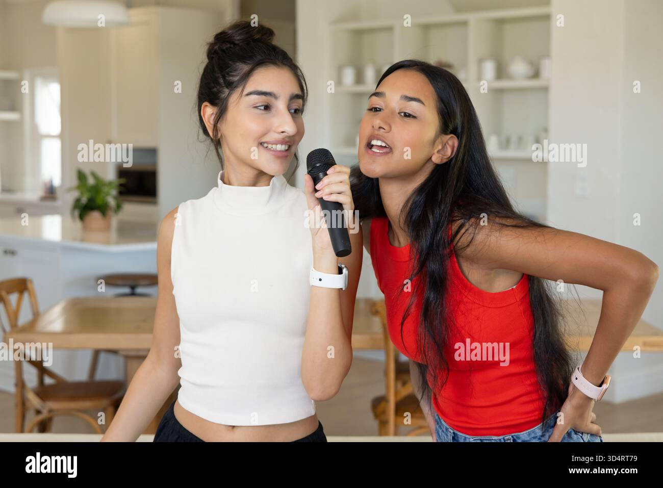Chanter diverses amies féminines debout dans la cuisine moderne de la maison et la salle à manger, avec microphone Banque D'Images