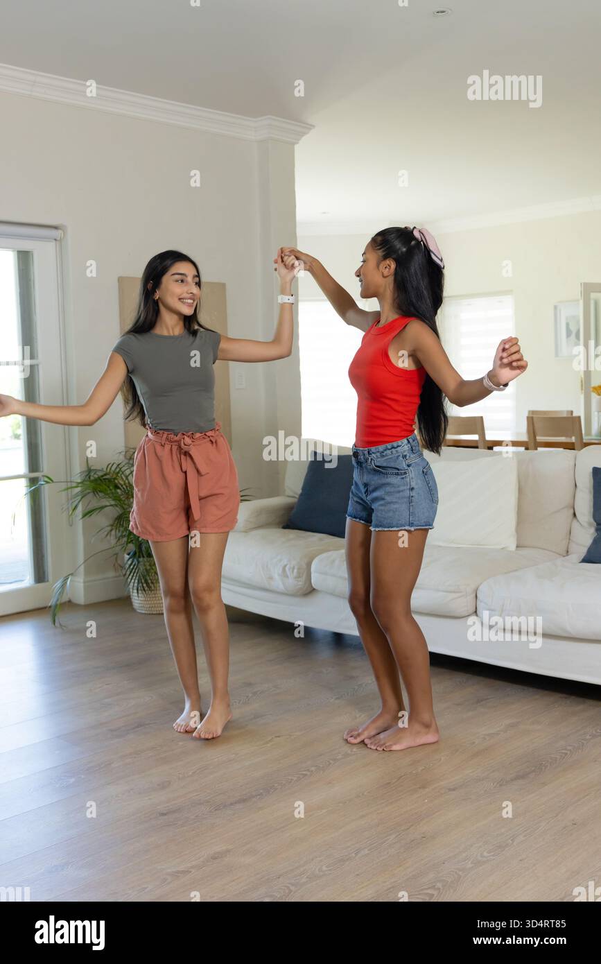 Danser diverses amies féminines se tenant la main et tourbillonnant dans un salon lumineux, avec canapé blanc Banque D'Images