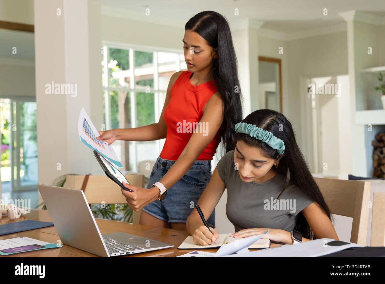 Collaboration de diverses amies féminines arrangeant des échantillons de couleurs et écrivant dans l'espace de travail, avec un ordinateur portable Banque D'Images