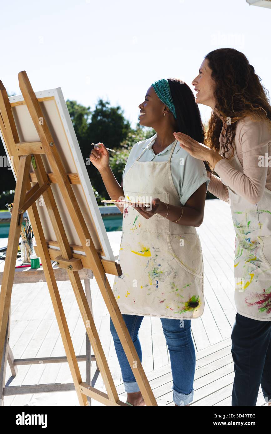 Enseignant et étudiant divers peignant ensemble sur la terrasse au bord de la piscine, avec chevalet et palette de peinture Banque D'Images