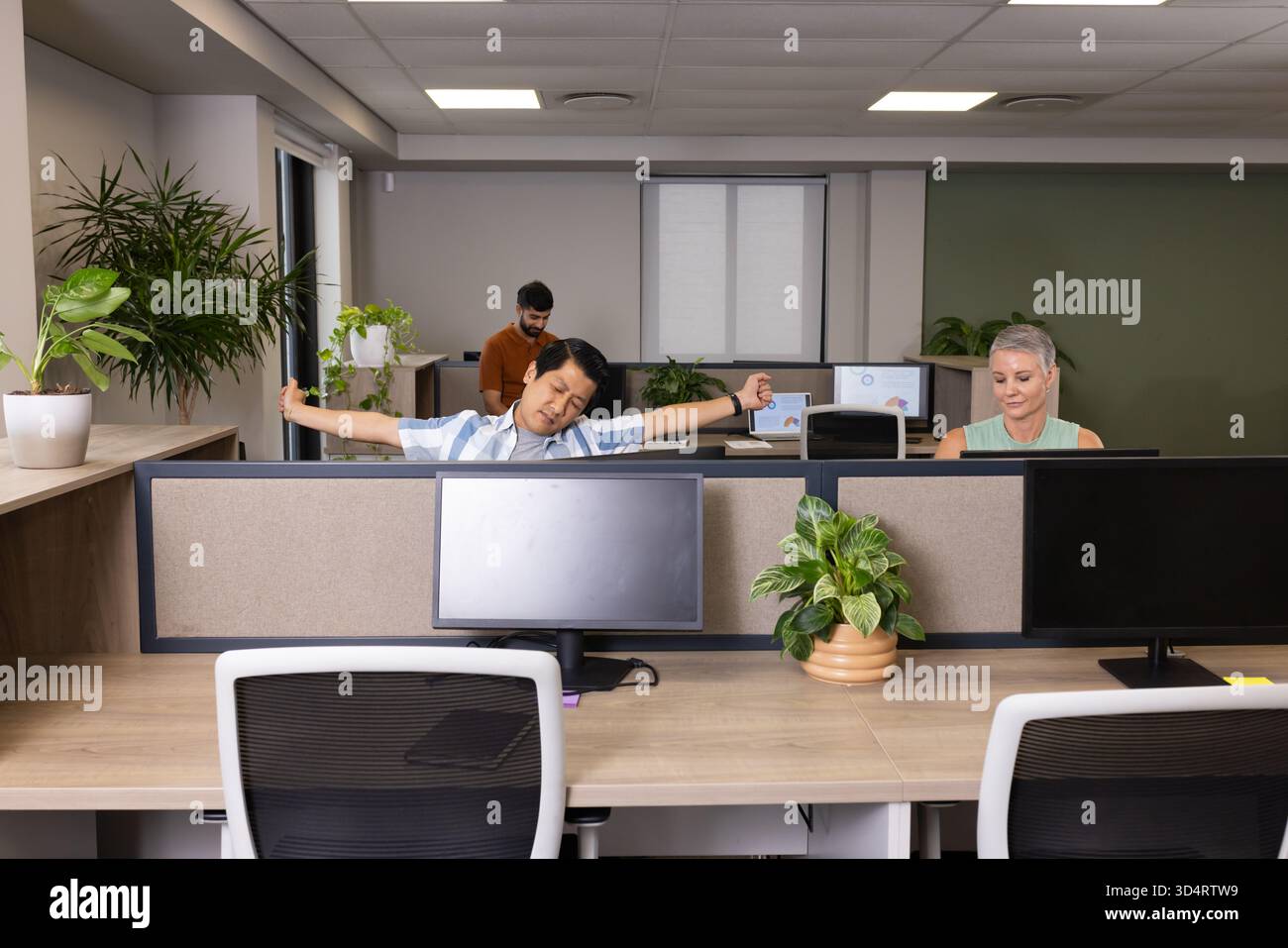 Étirer l'homme indien asiatique penché en arrière à un bureau ouvert, avec des écrans d'ordinateur Banque D'Images