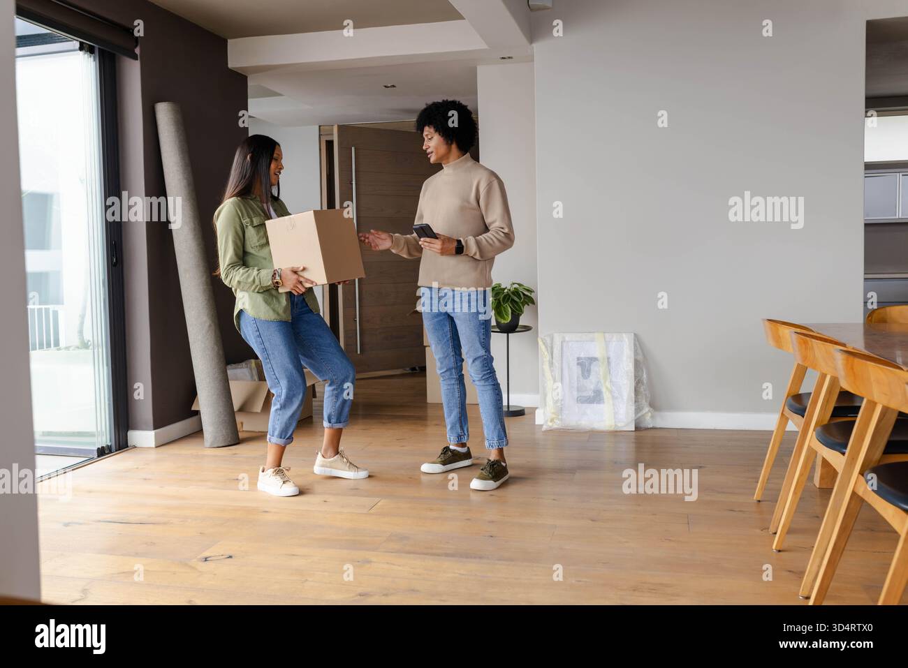 Couple diversifié déballage dans un espace repas de vie ouvert, tenant une boîte en carton et un smartphone Banque D'Images