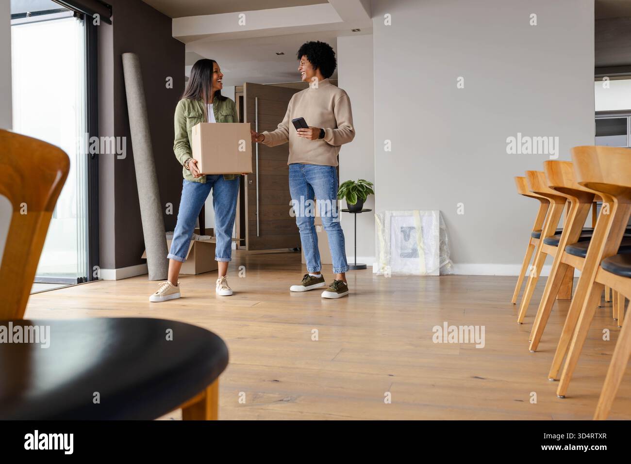 Tenant le smartphone et portant la boîte mobile, diverses amies féminines debout dans un appartement moderne Banque D'Images