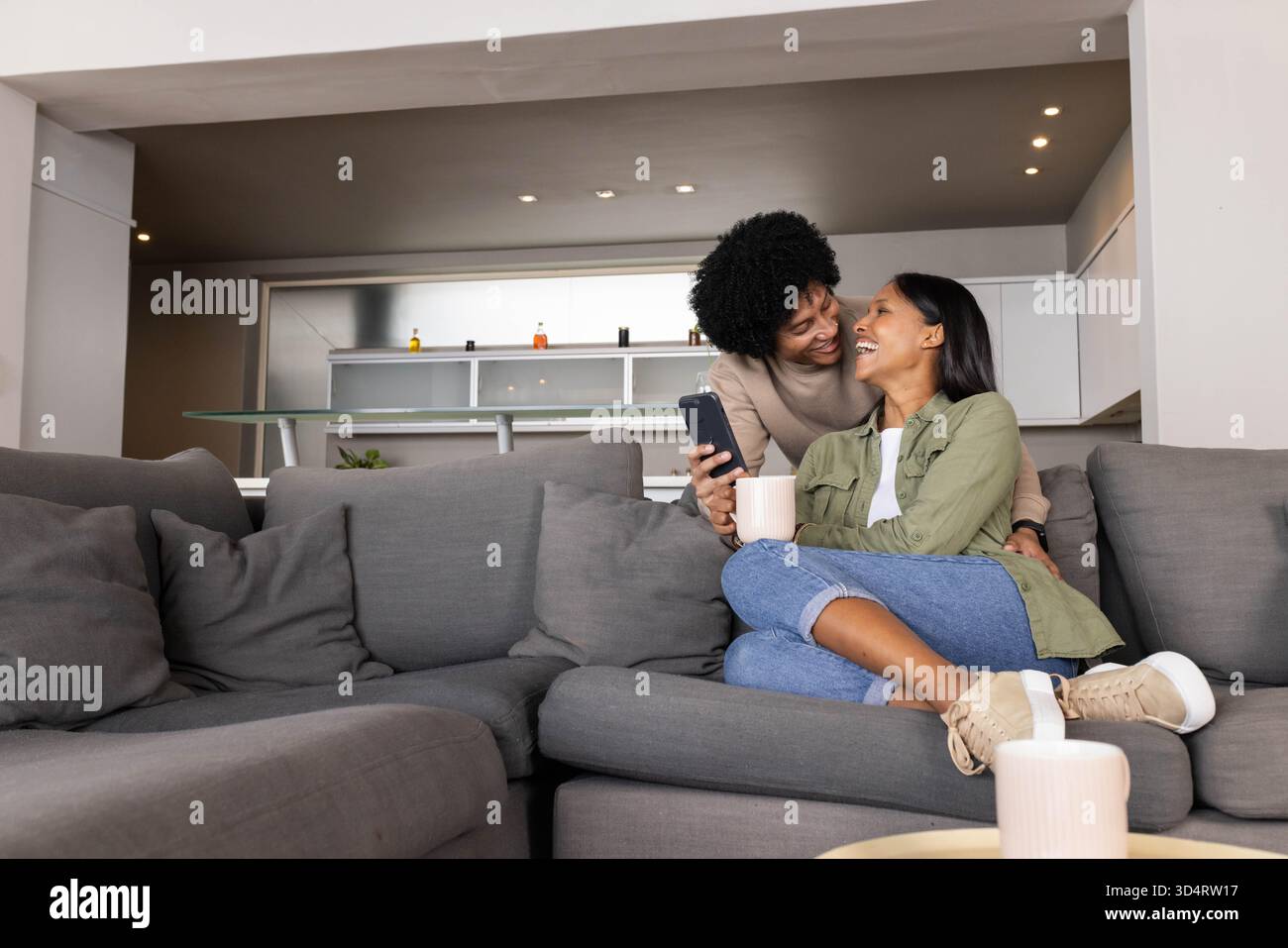 Divers partenaires féminins partageant le café et le smartphone sur le canapé dans le salon moderne Banque D'Images