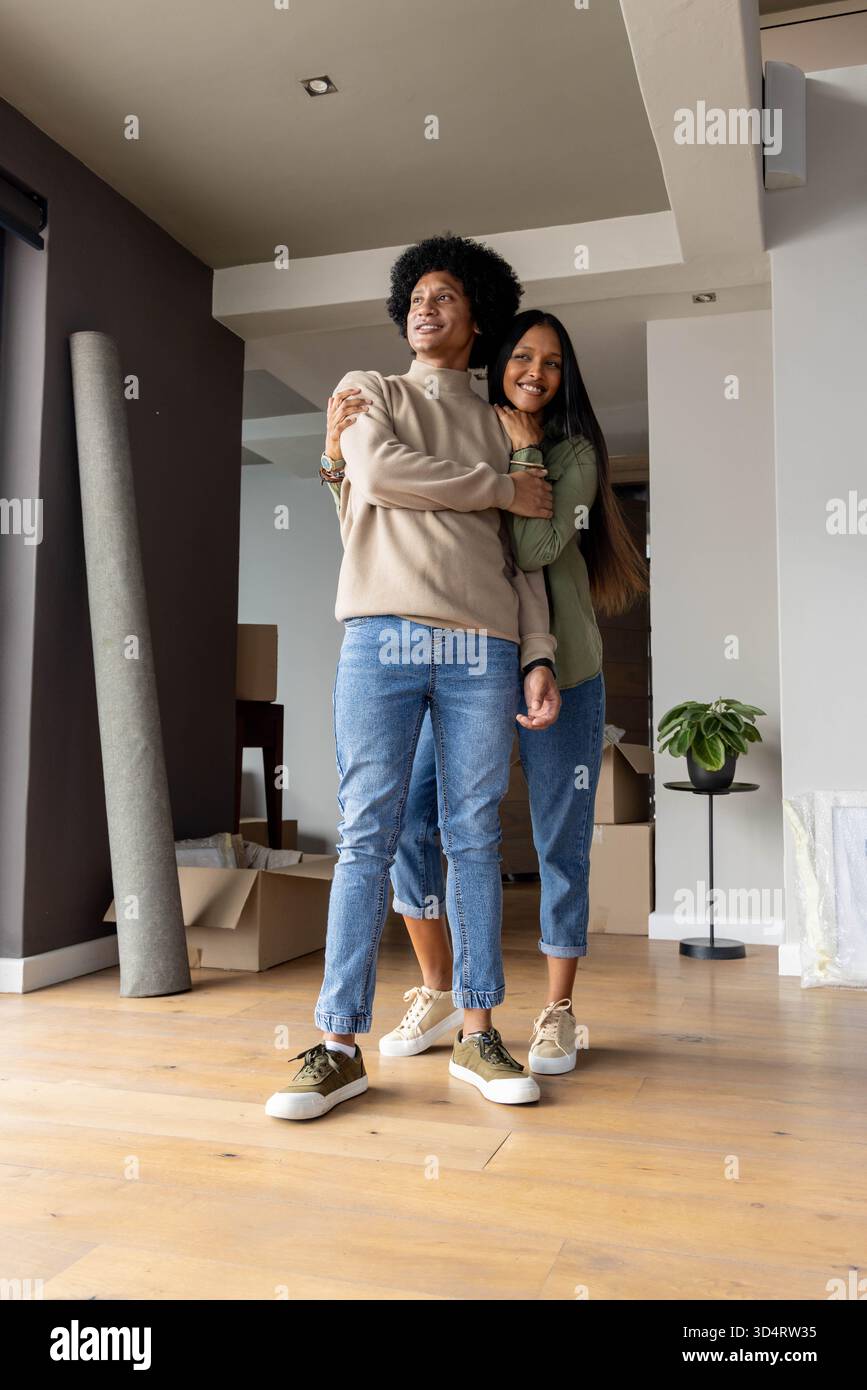 Embrassant un couple diversifié debout dans un salon presque vide, avec des boîtes mobiles et des plantes en pot Banque D'Images