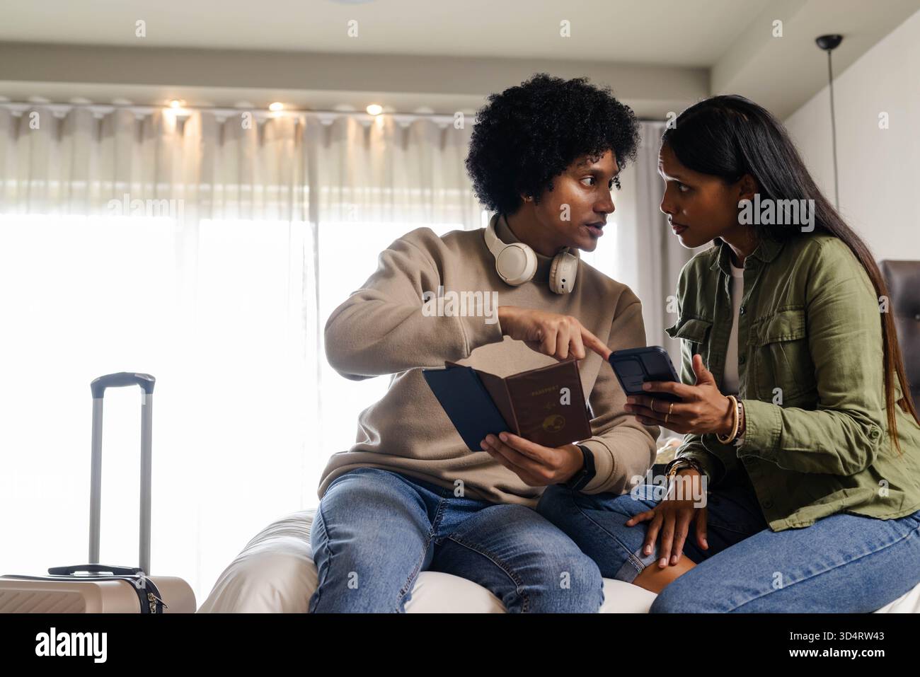 Planification de couple diversifié examinant le passeport sur le lit dans la chambre d'hôtel, avec smartphone et valise Banque D'Images