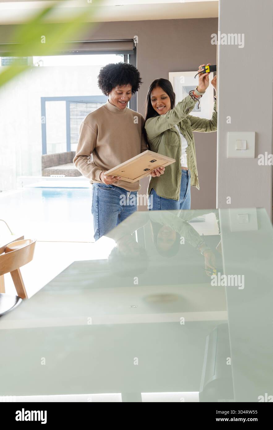 Cadre d'image suspendu de couple diversifié dans l'intérieur de la maison moderne, en utilisant un mètre à ruban jaune Banque D'Images