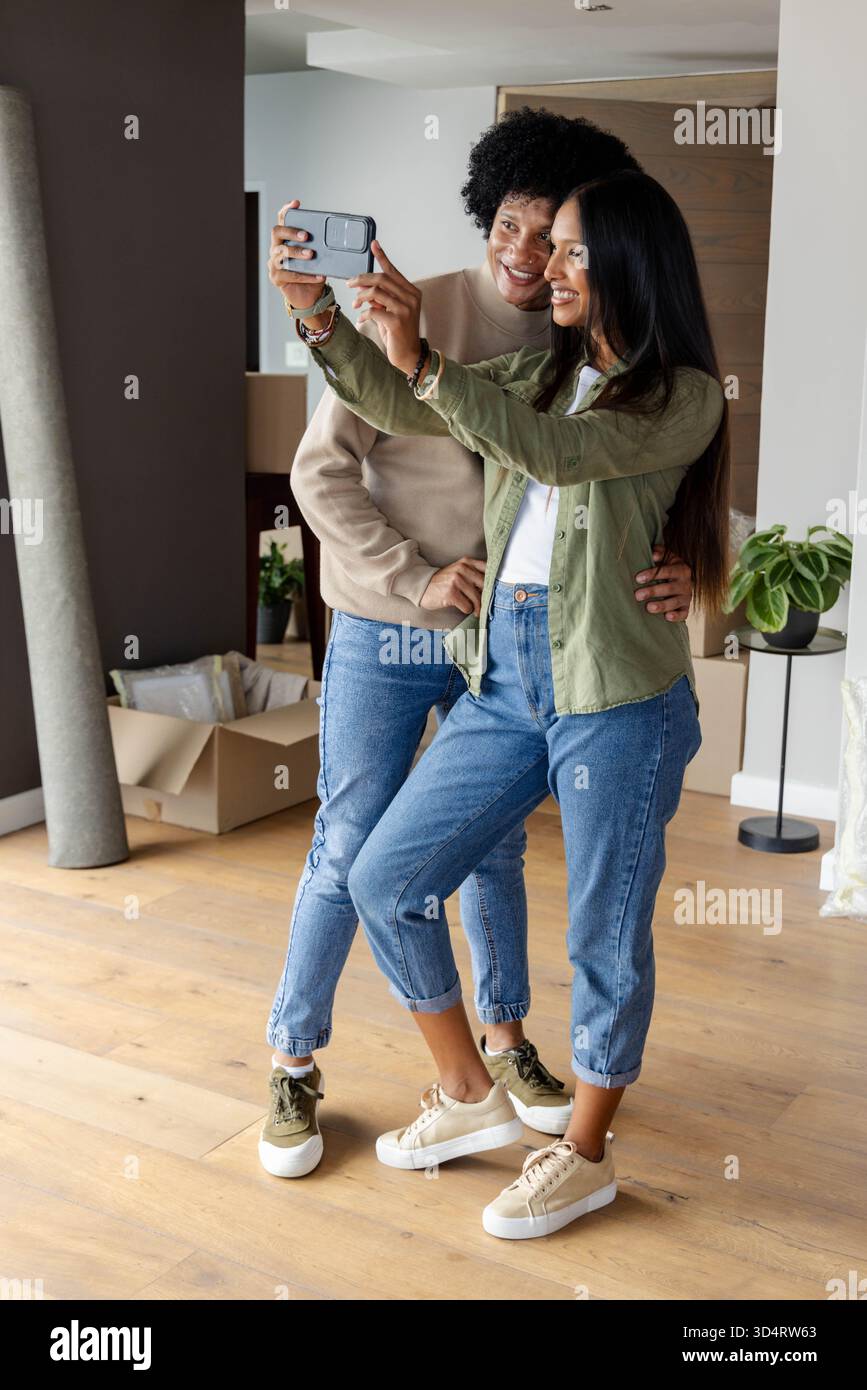 Prise selfie couple diversifié debout dans un appartement non meublé, avec smartphone et boîtes mobiles Banque D'Images