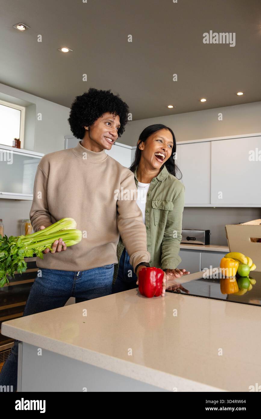 Couple diversifié préparant des légumes sur l'îlot de cuisine, avec du céleri, des poivrons et four grille-pain Banque D'Images