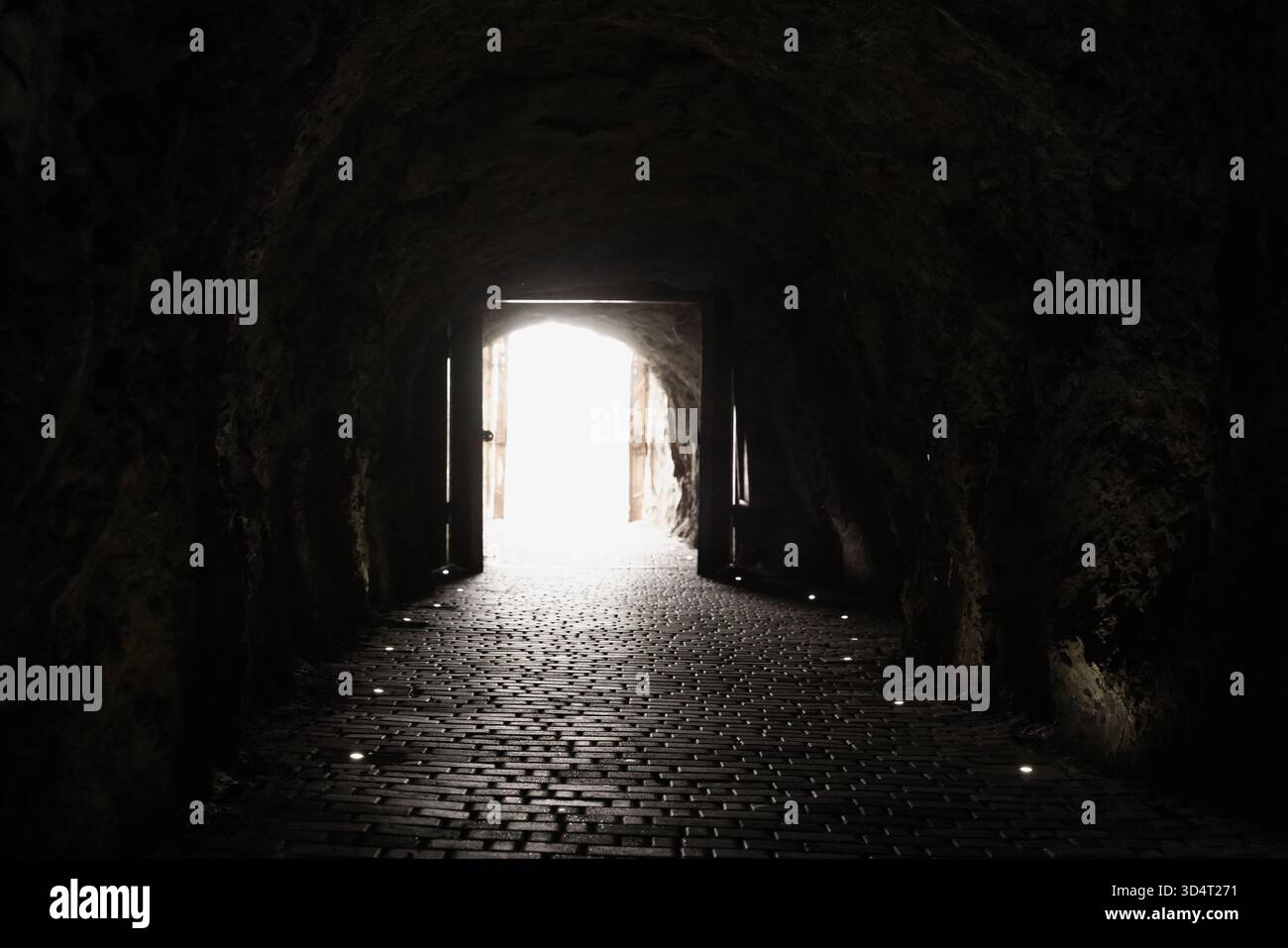 Un tunnel souterrain sombre avec des murs en pierre rugueuse et une sortie incandescente à l'extrémité. Le sol pavé guide le chemin vers la lumière du jour, évoquant le mystère, adve Banque D'Images