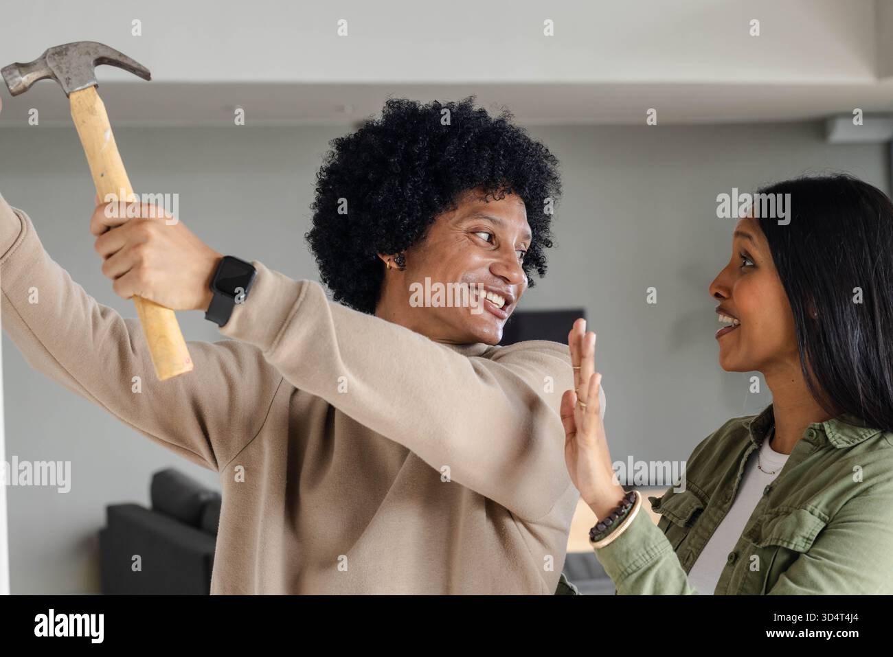 Divers amis balançant le marteau et levant la main dans le salon moderne, avec ordinateur portable et canapé Banque D'Images