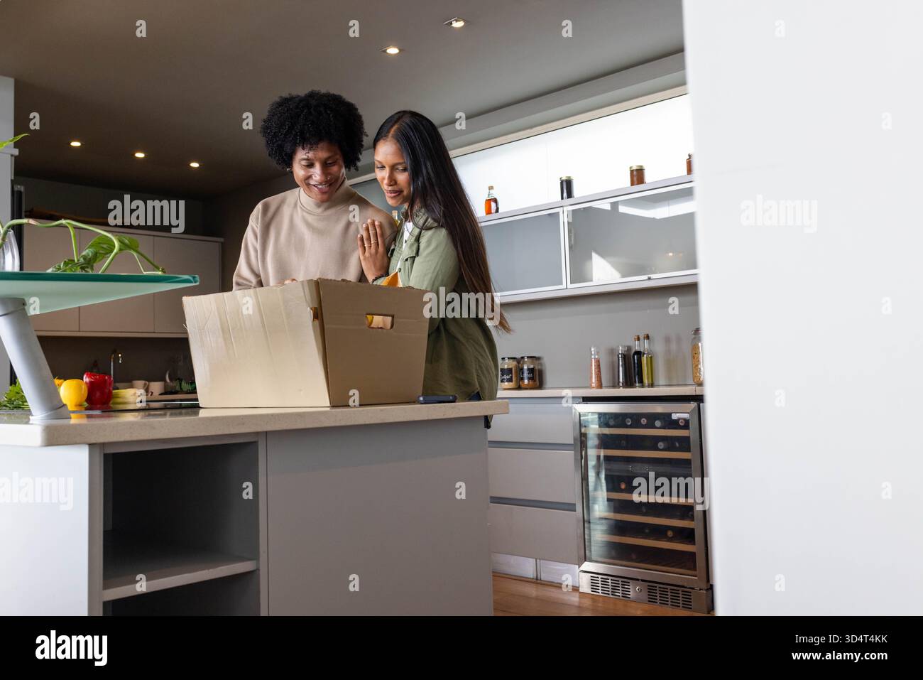 Sourire couple diversifié déballage de l'épicerie à l'îlot de cuisine, avec boîte en carton et poivrons Banque D'Images