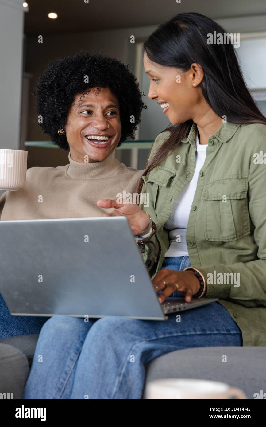 Chatter divers amis assis sur le canapé dans le salon moderne, avec ordinateur portable argenté et tasse à café Banque D'Images