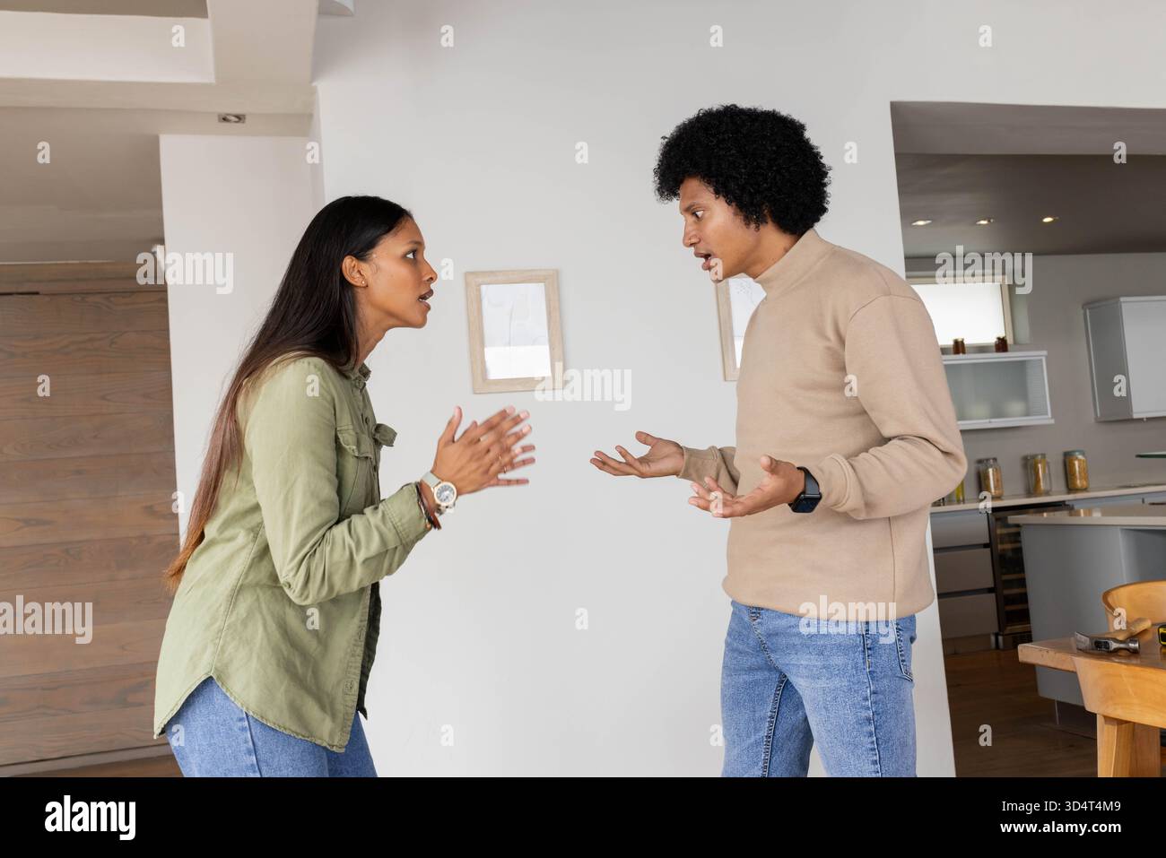 Argumentant un couple diversifié debout dans un intérieur de maison ouvert, avec des armoires blanches et une porte en bois Banque D'Images