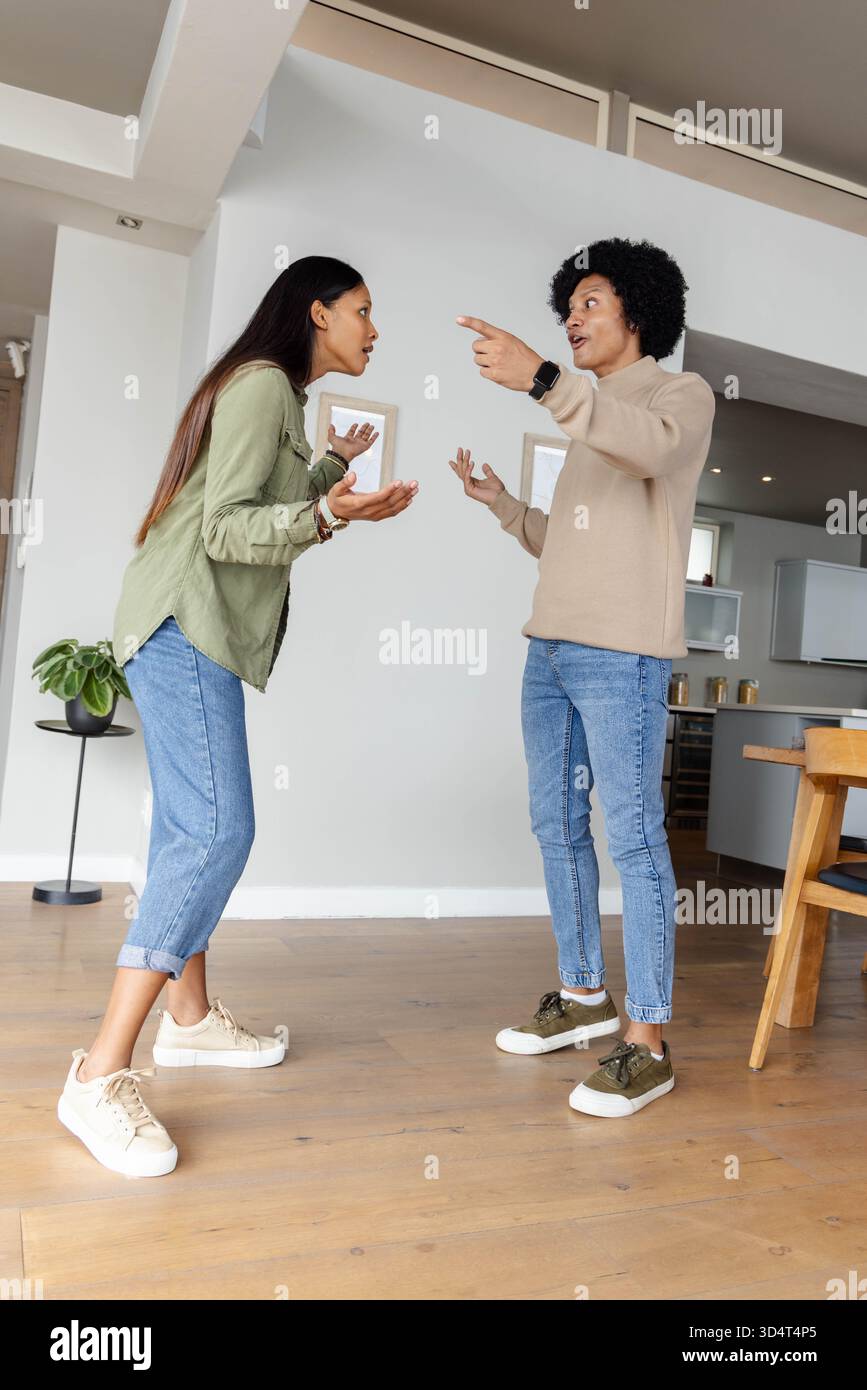 Argumentant couple diversifié debout dans la maison ouverte, avec smartwatch et plante en pot Banque D'Images