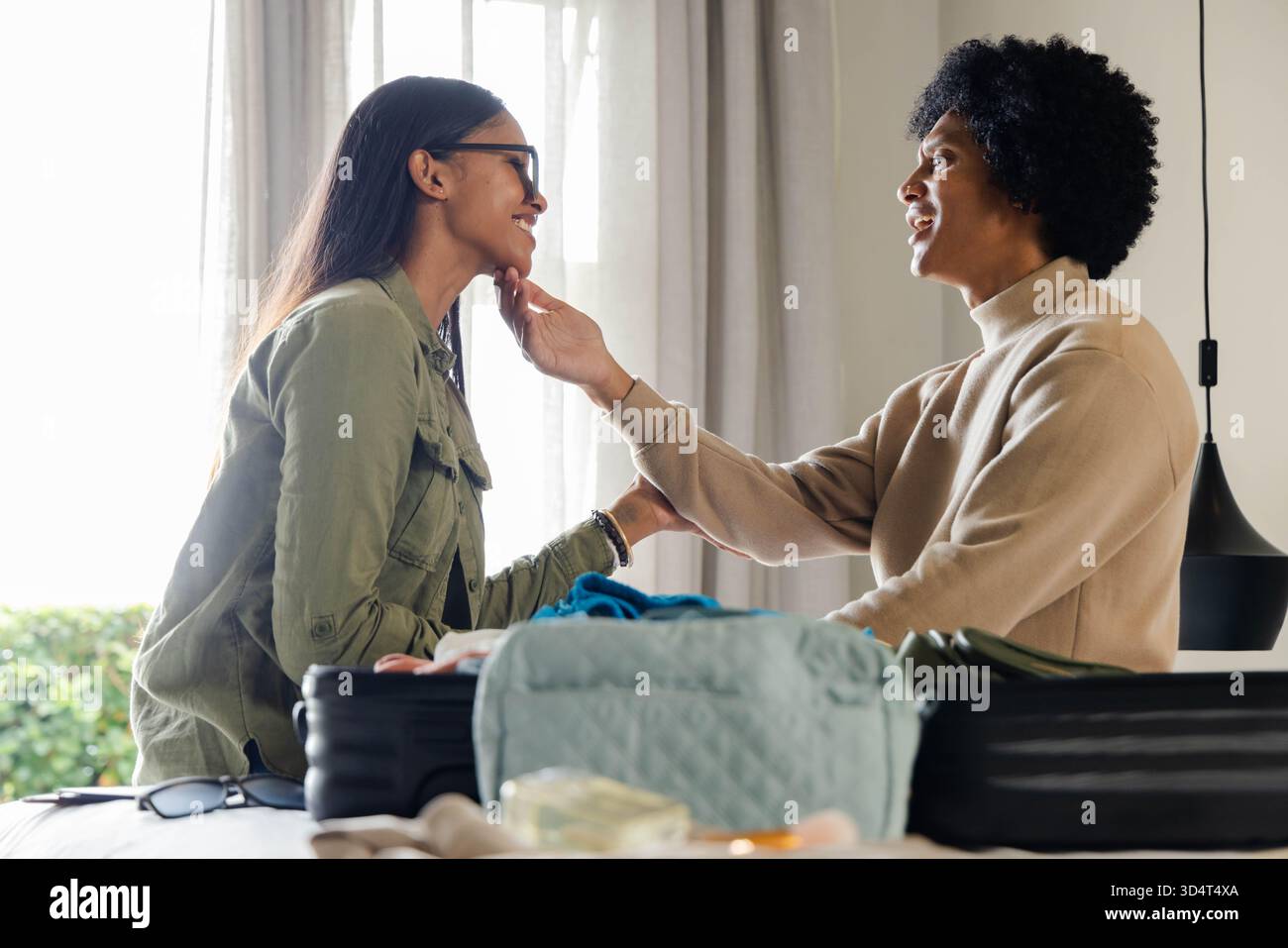 Homme souriant et femme indienne échangeant contact tout en emballant des articles à la maison, avec valise noire ouverte Banque D'Images