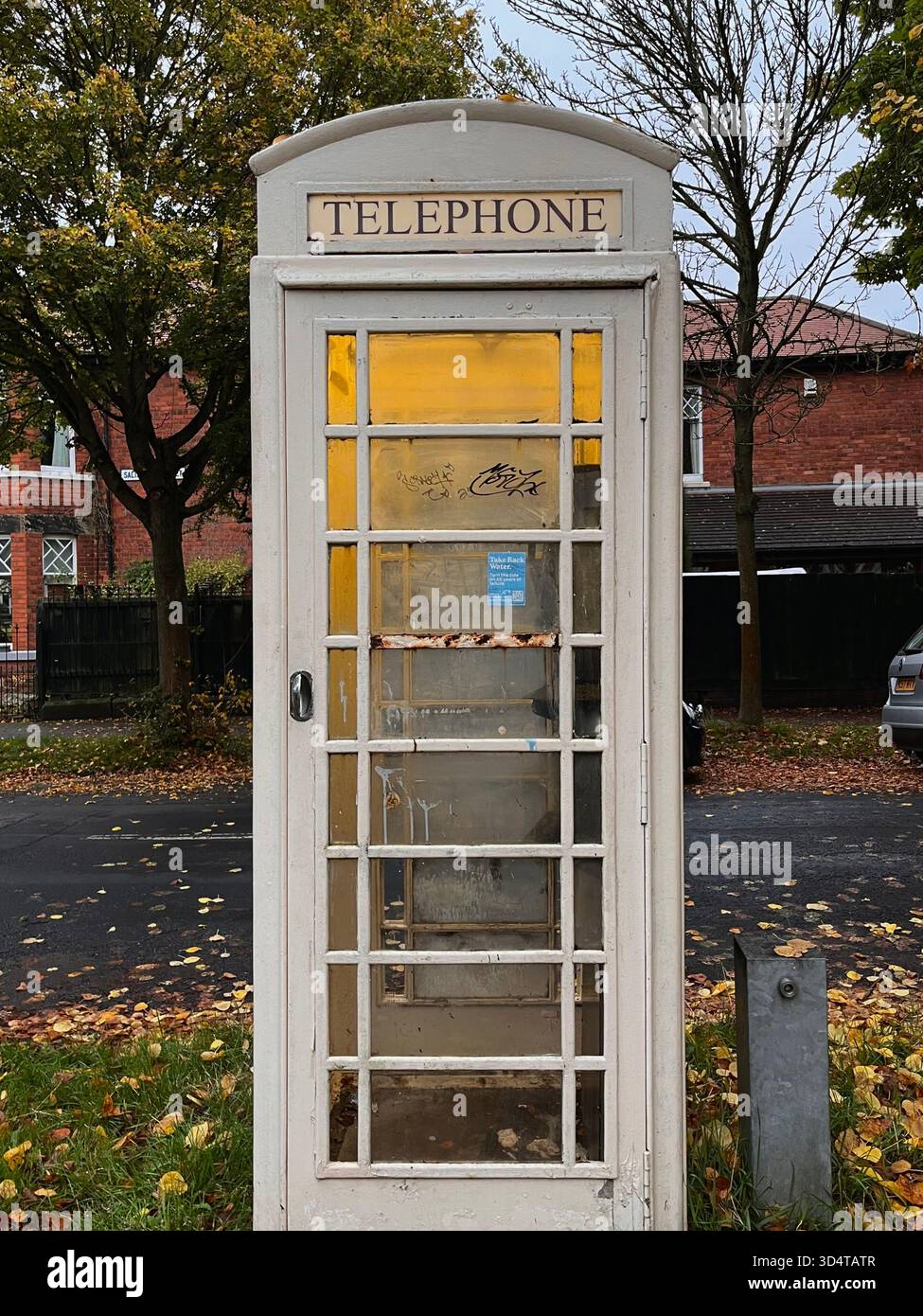 Une cabine téléphonique britannique classique entourée de feuilles d'automne dans un quartier calme de Hull. Symbole emblématique du patrimoine et du design britanniques. - Image de stock capturée avec un smartphone