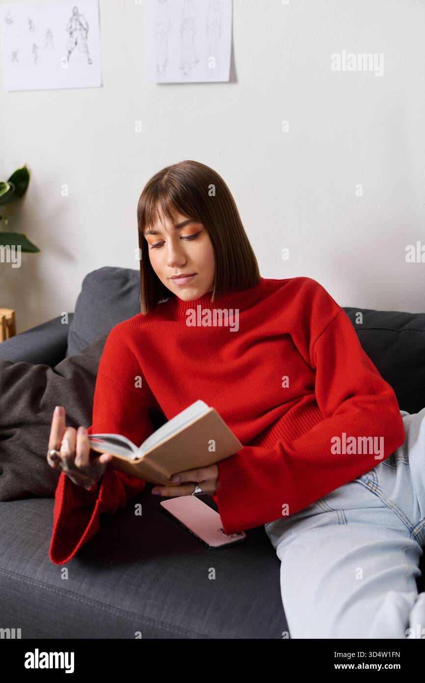 Jeune femme en pull rouge aime lire à la maison, entourée de croquis et de créativité. Banque D'Images