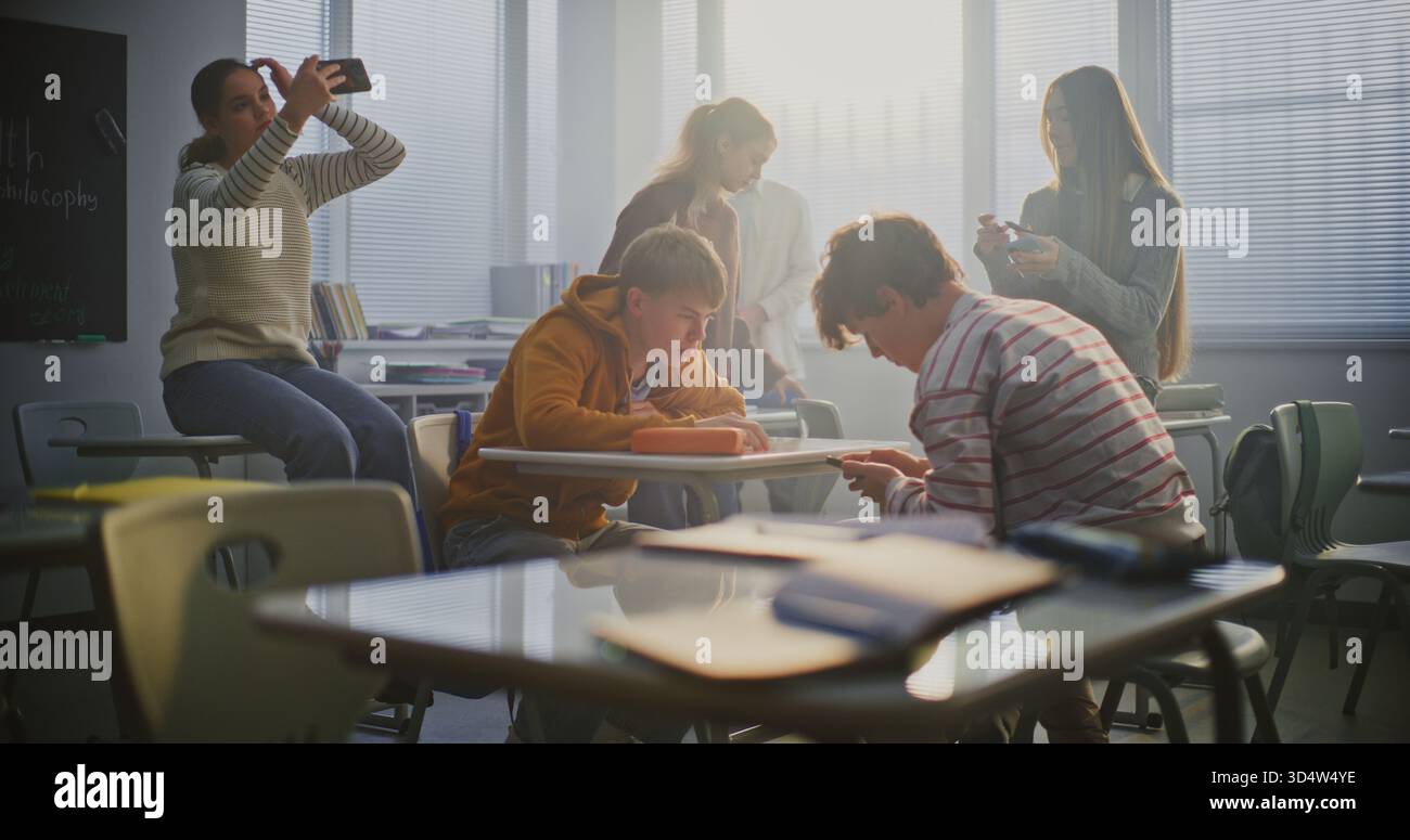 Deux étudiants masculins luttent au bureau pendant la pause, entourés de camarades de classe qui encouragent et filment sur smartphone. Concept de l'énergie des jeunes, de la compétition, de l'amitié et de l'interaction sociale. Tir statique. Banque D'Images
