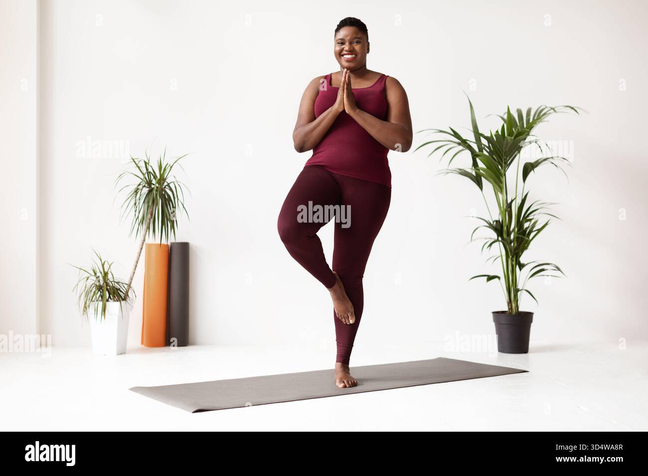 Femme noire joyeuse pratiquant le yoga dans Fitness Studio tout en profitant de sa routine quotidienne Banque D'Images