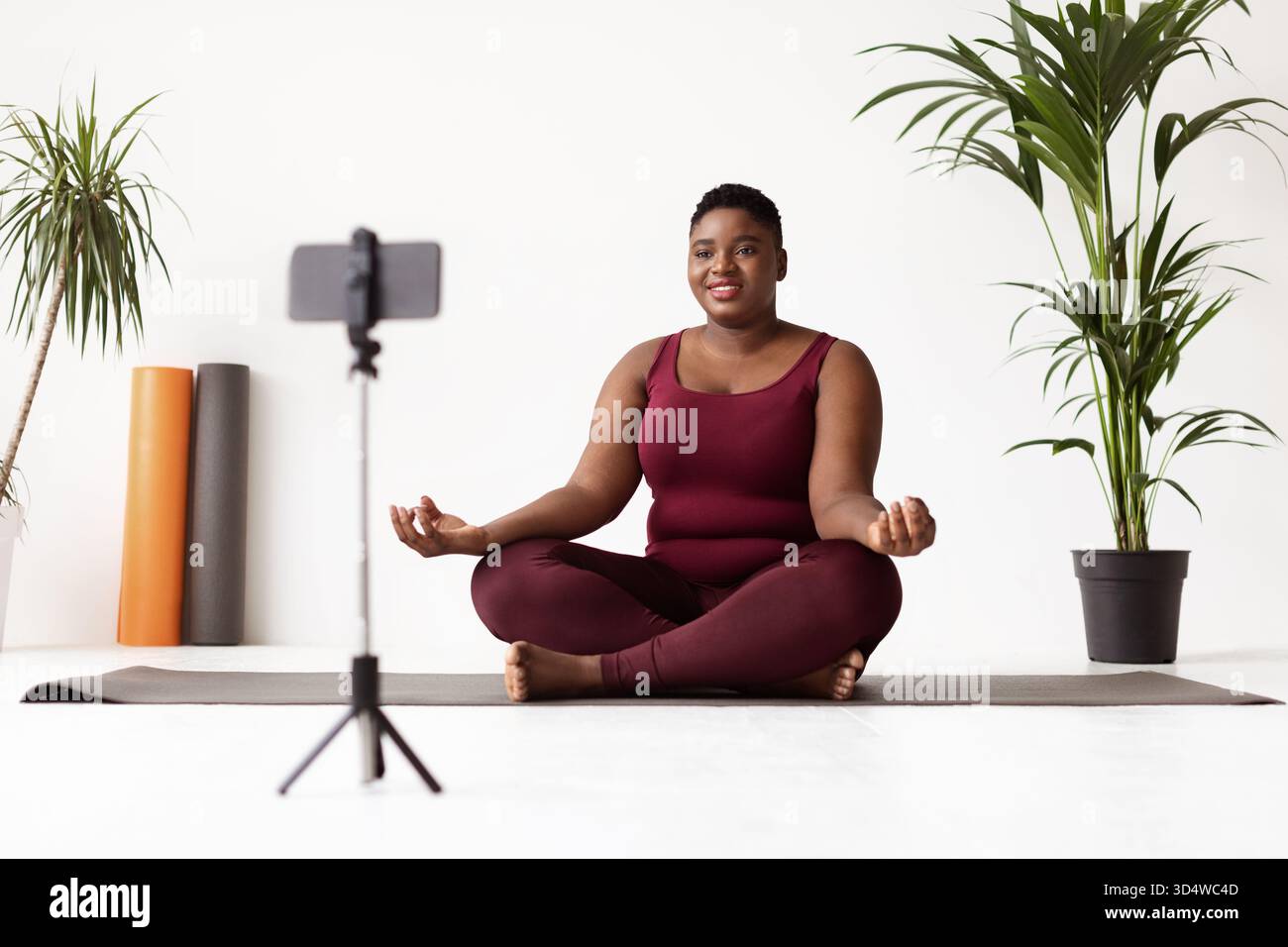 Plump Black Lady pratiquant le yoga à la maison pendant le cours en ligne dans des vêtements de sport confortables Banque D'Images