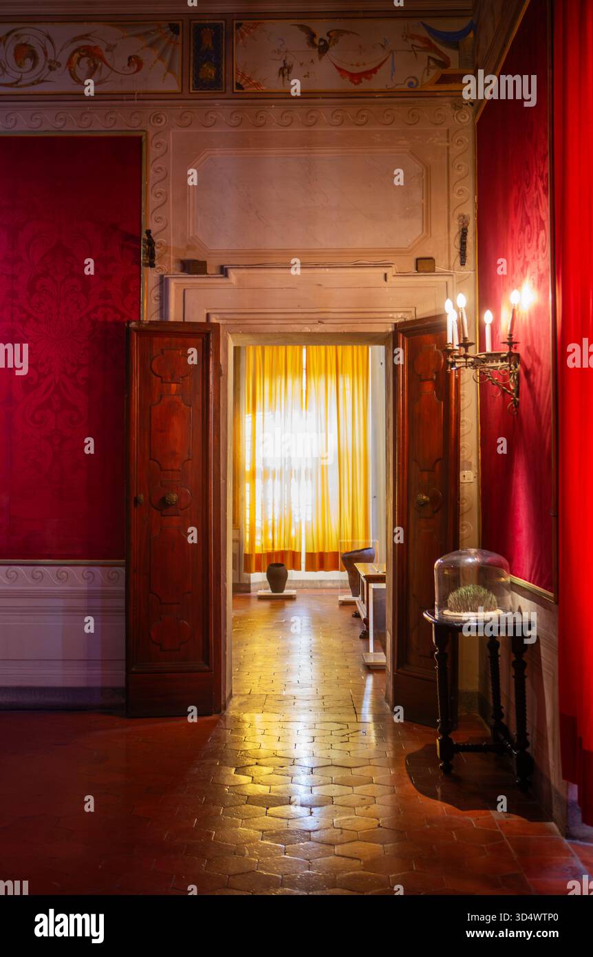 Couloir élégant à l'intérieur du palais historique avec murs en velours rouge portes en bois et lumière douce du soleil à travers des rideaux jaunes. Banque D'Images