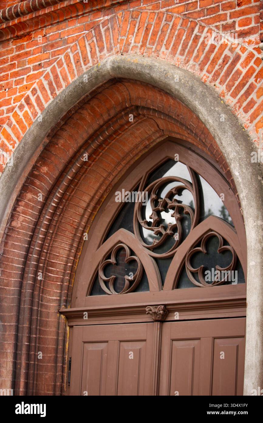 Porte voûtée de style gothique avec tracés décoratifs en bois et façade en briques rouges. Détail architectural d'un bâtiment historique. Banque D'Images